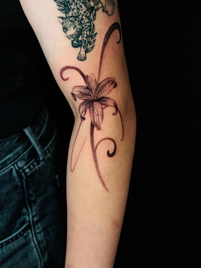 Tattoo of a large, detailed lily flower with curling tendrils on a person's forearm.