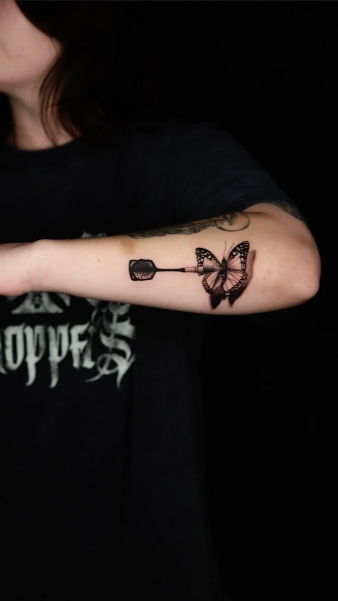 Tattoo of a butterfly and an anvil on a person's forearm.