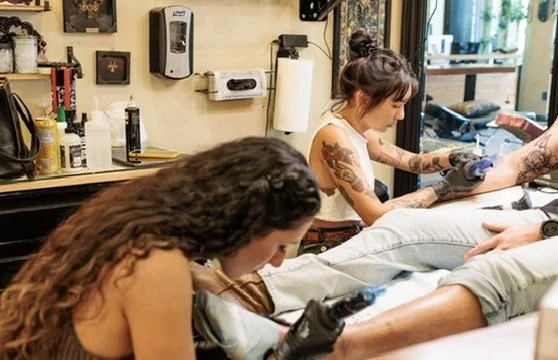 Two tattoo artists working on clients in a tattoo shop.