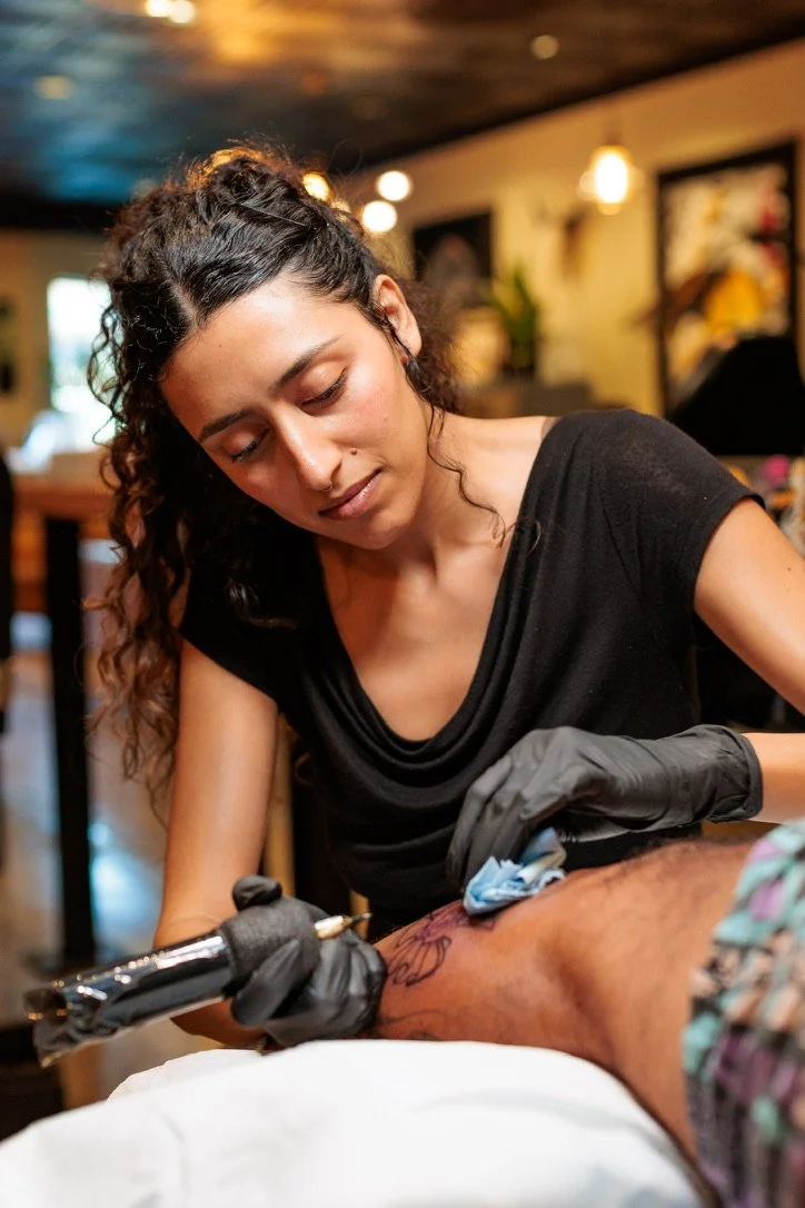 Woman tattooing a man's arm in a tattoo shop.