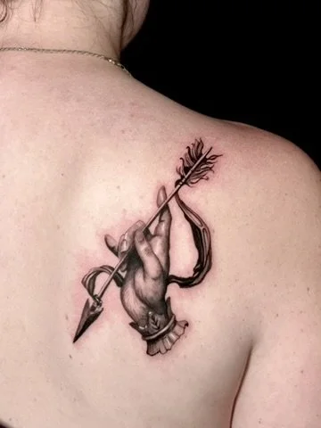 Tattoo of a hand holding an arrow on a person's shoulder.
