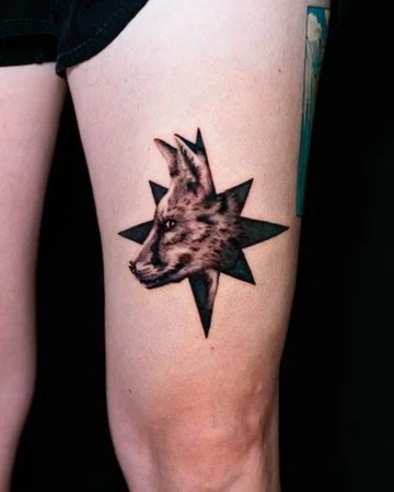 Tattoo of a dog's head on a person's thigh with a starburst background.
