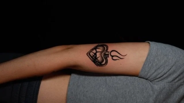 Tattoo of a heart with flames on a person's inner upper arm.
