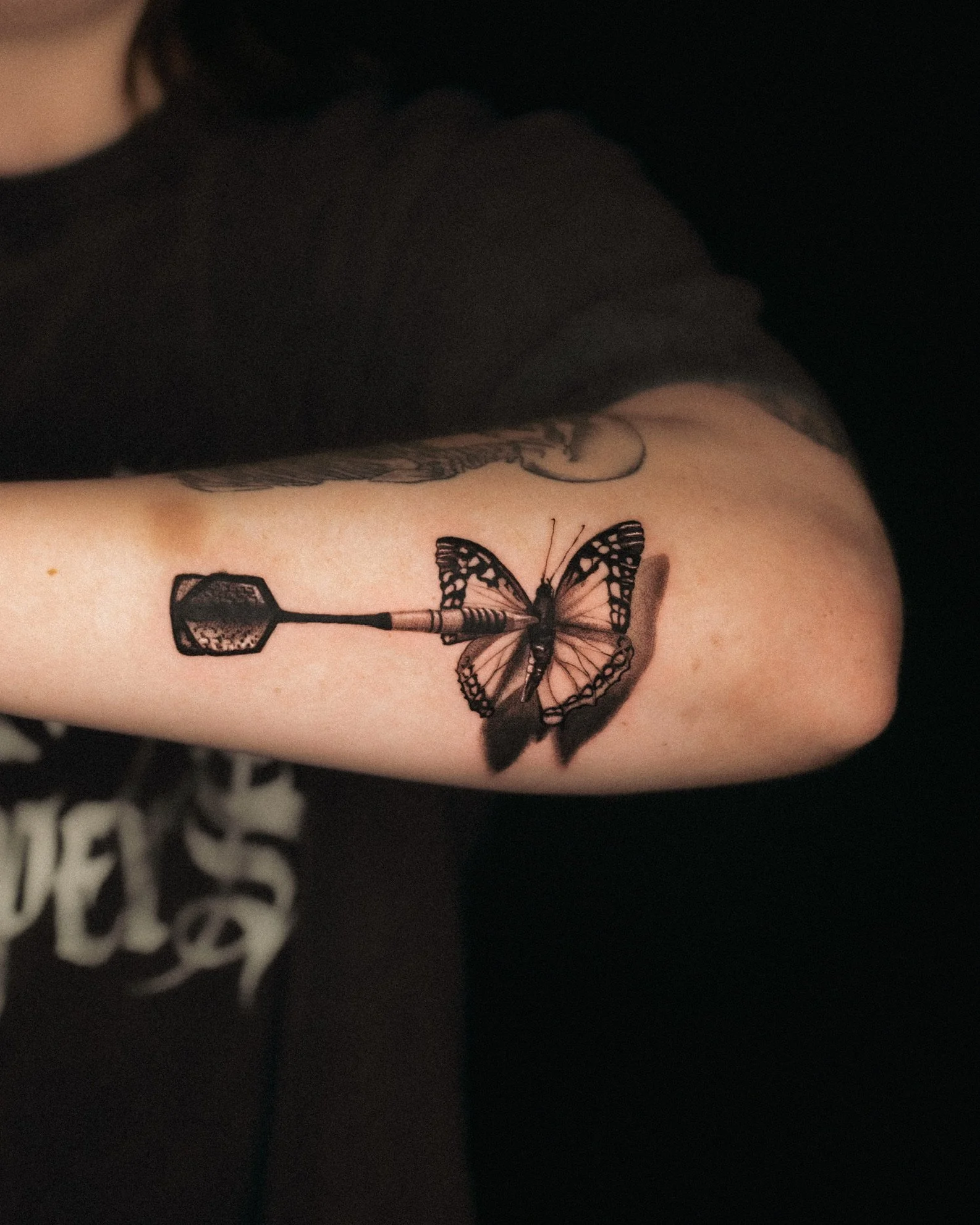 Tattoo of a butterfly with a dart through its body on a person's arm.