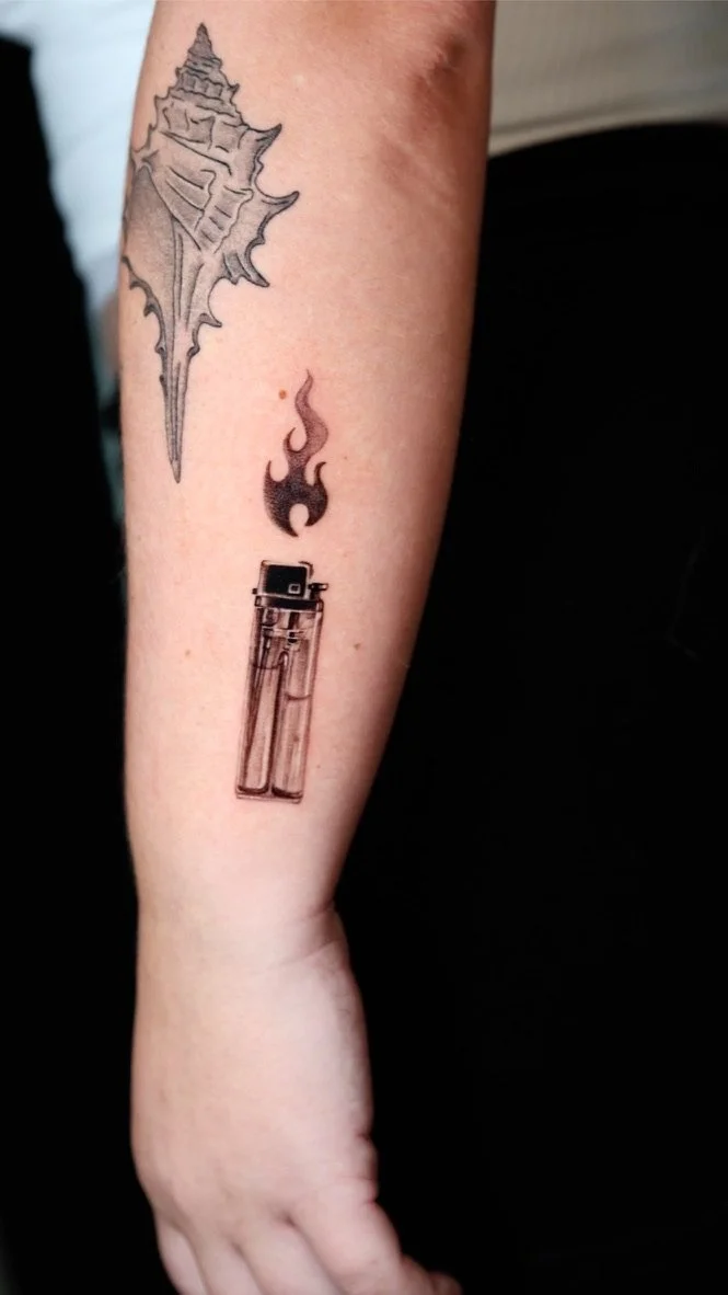 Tattoo of a dragon, a flame, and a lighter on a person's forearm.