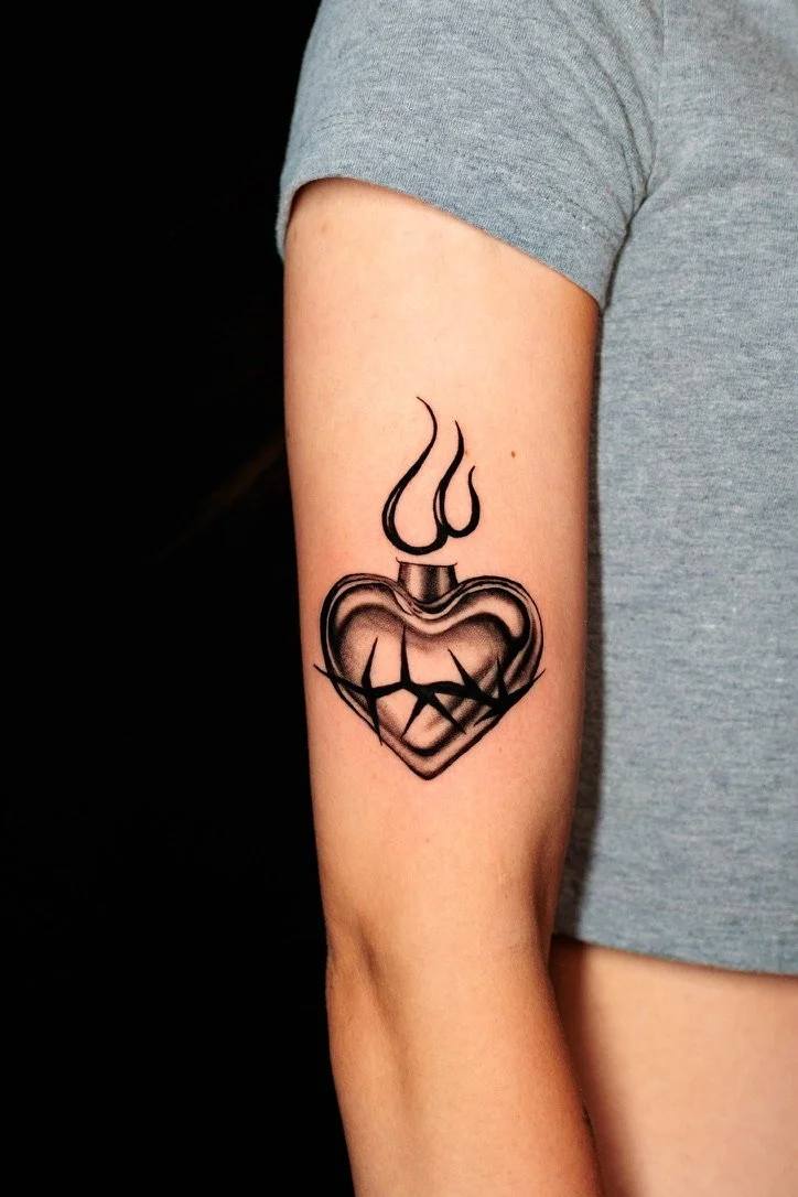 Tattoo of a broken heart shaped perfume bottle with steam or smoke rising from it, on a person's upper arm.