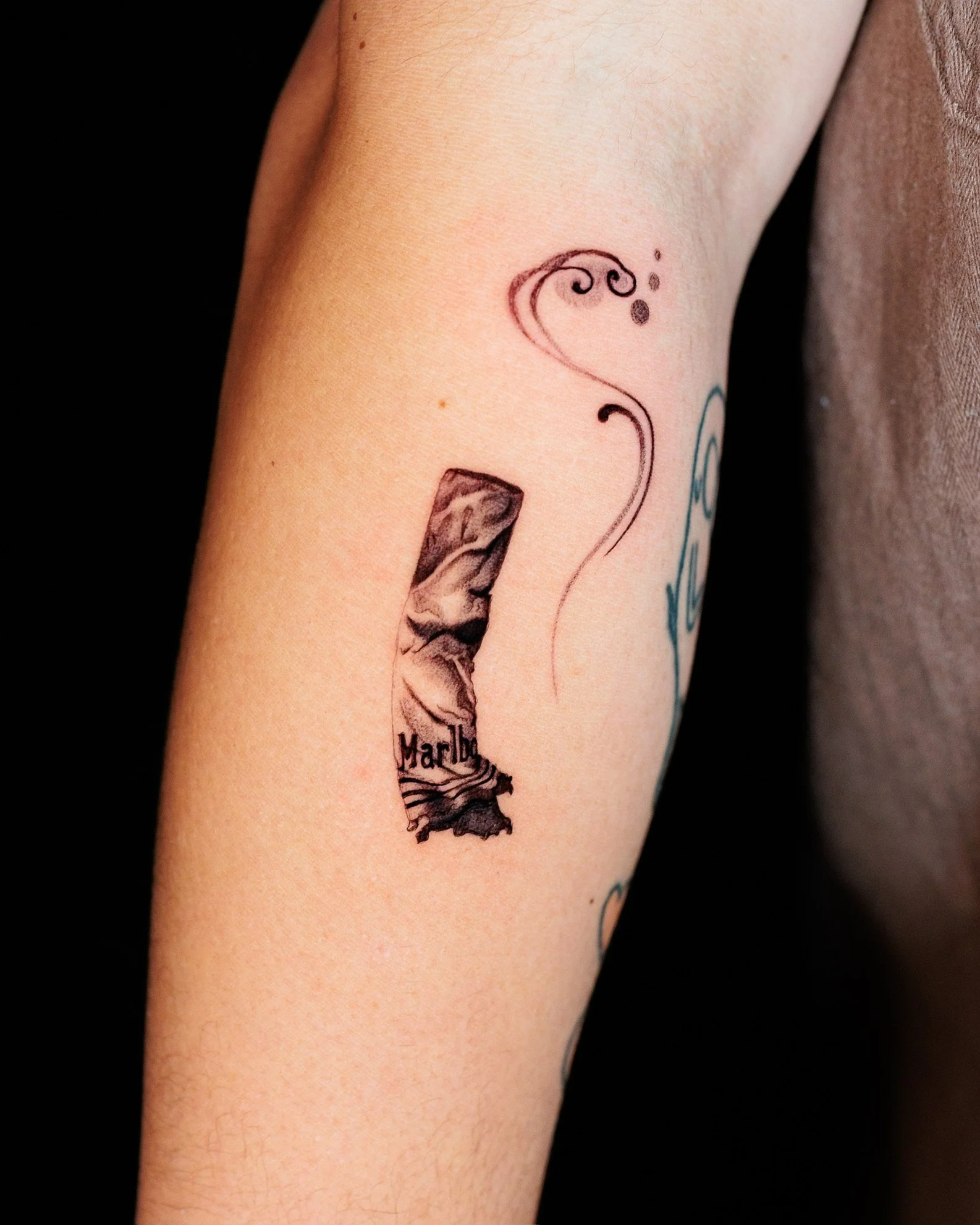 Close-up of a person's inner forearm with a small Marlin tobacco cigarette tattoo.
