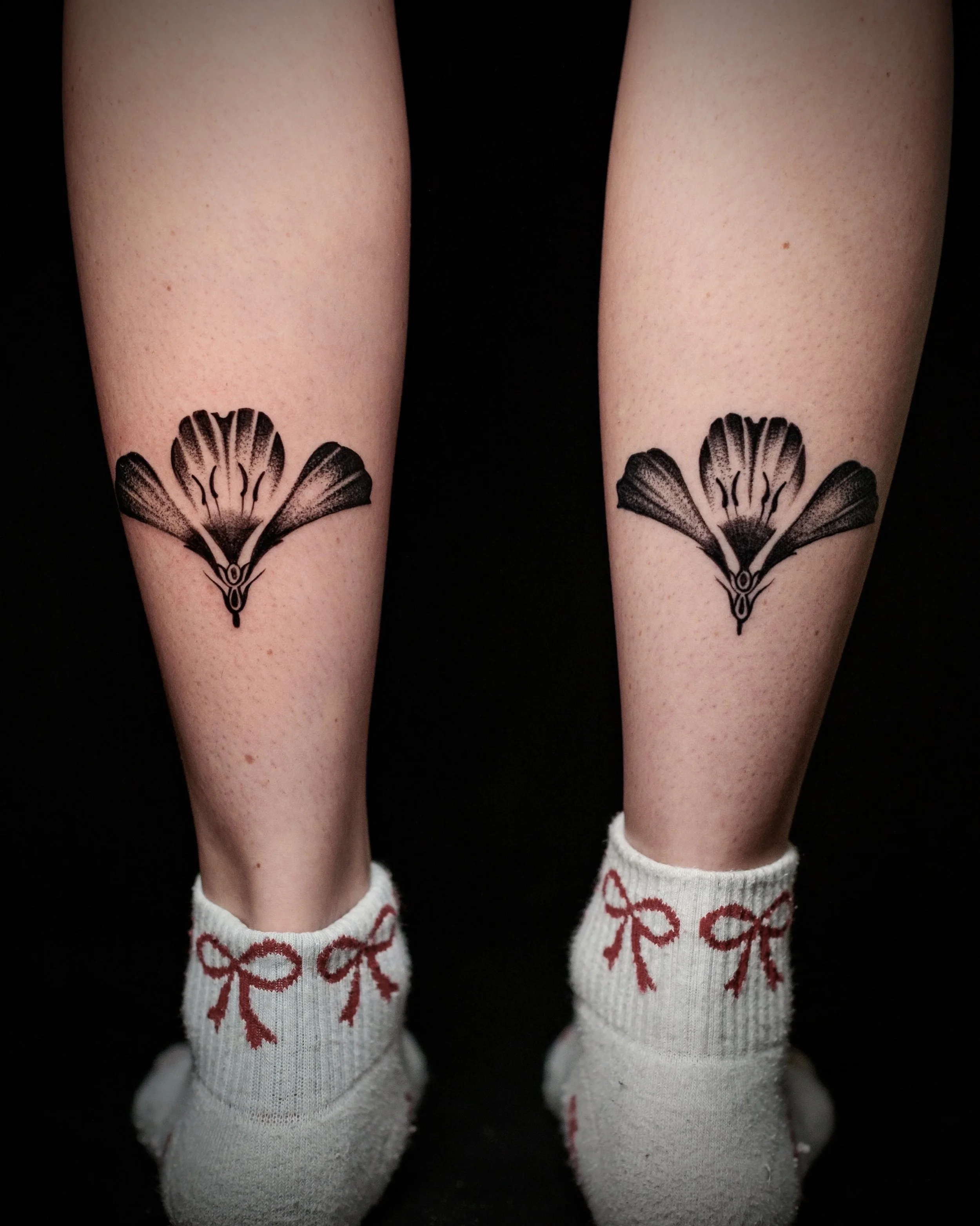 Two legs with matching butterfly tattoos on the calves and white socks with red bows, against a black background.