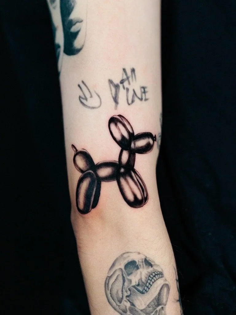 Tattoo of a balloon dog on the forearm, with the phrase 'You did' written above and a skull tattoo below.