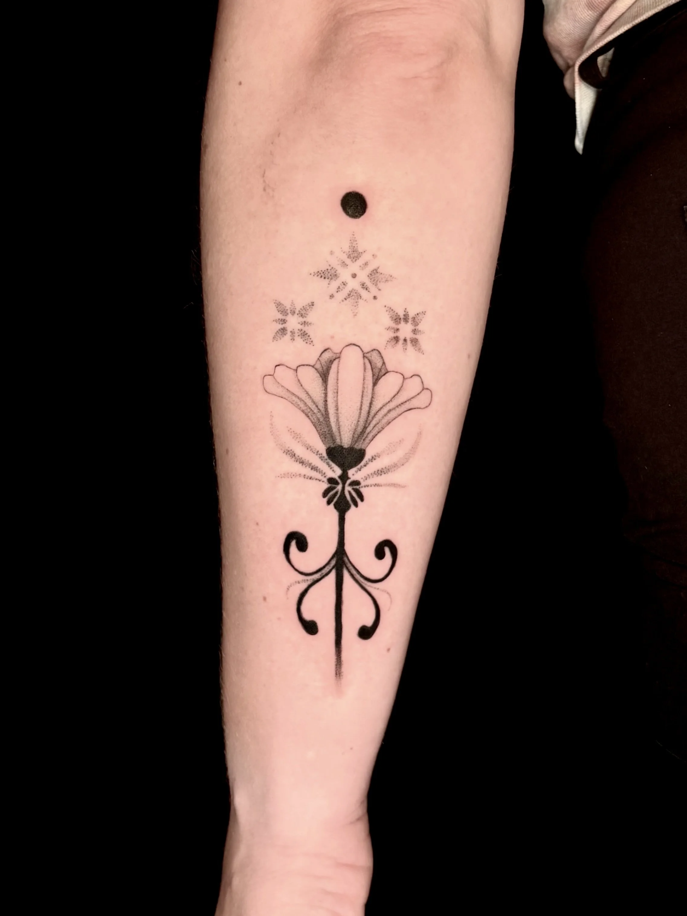 Tattoo of a flower with intricate details on the lower arm.