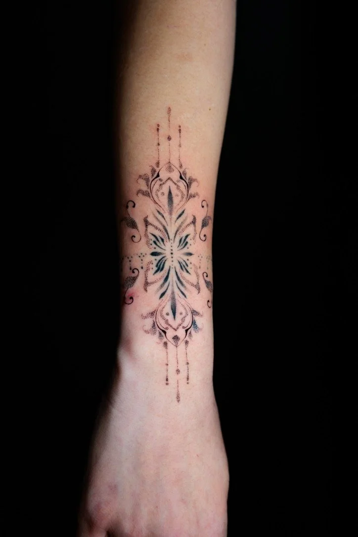 Black and gray floral tattoo design on inner forearm with symmetrical patterns and dotted accents.