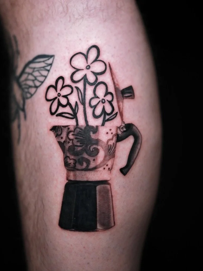 Tattoo of a moka pot with flowers growing out of it, depicted in black ink.