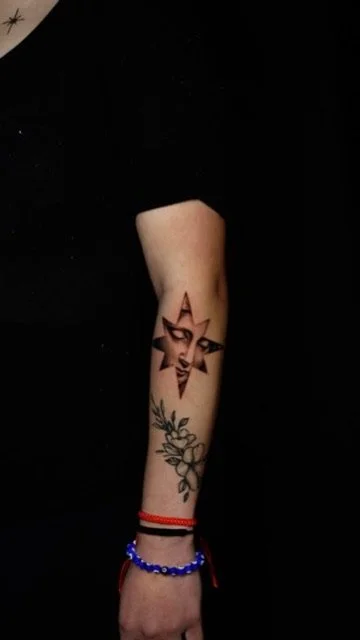 Tattoo of a star with a face inside on a person's forearm, along with additional floral designs below.