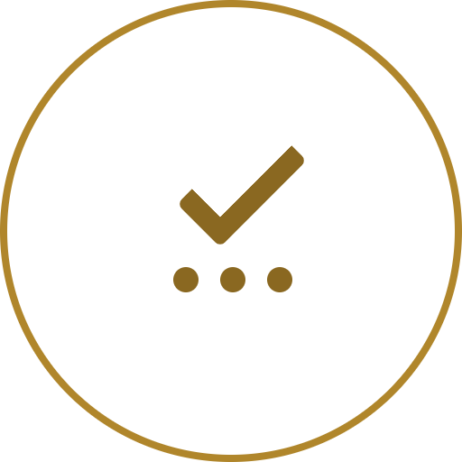 A white circular button with a gold border, featuring a brown checkmark and three small dots below it.