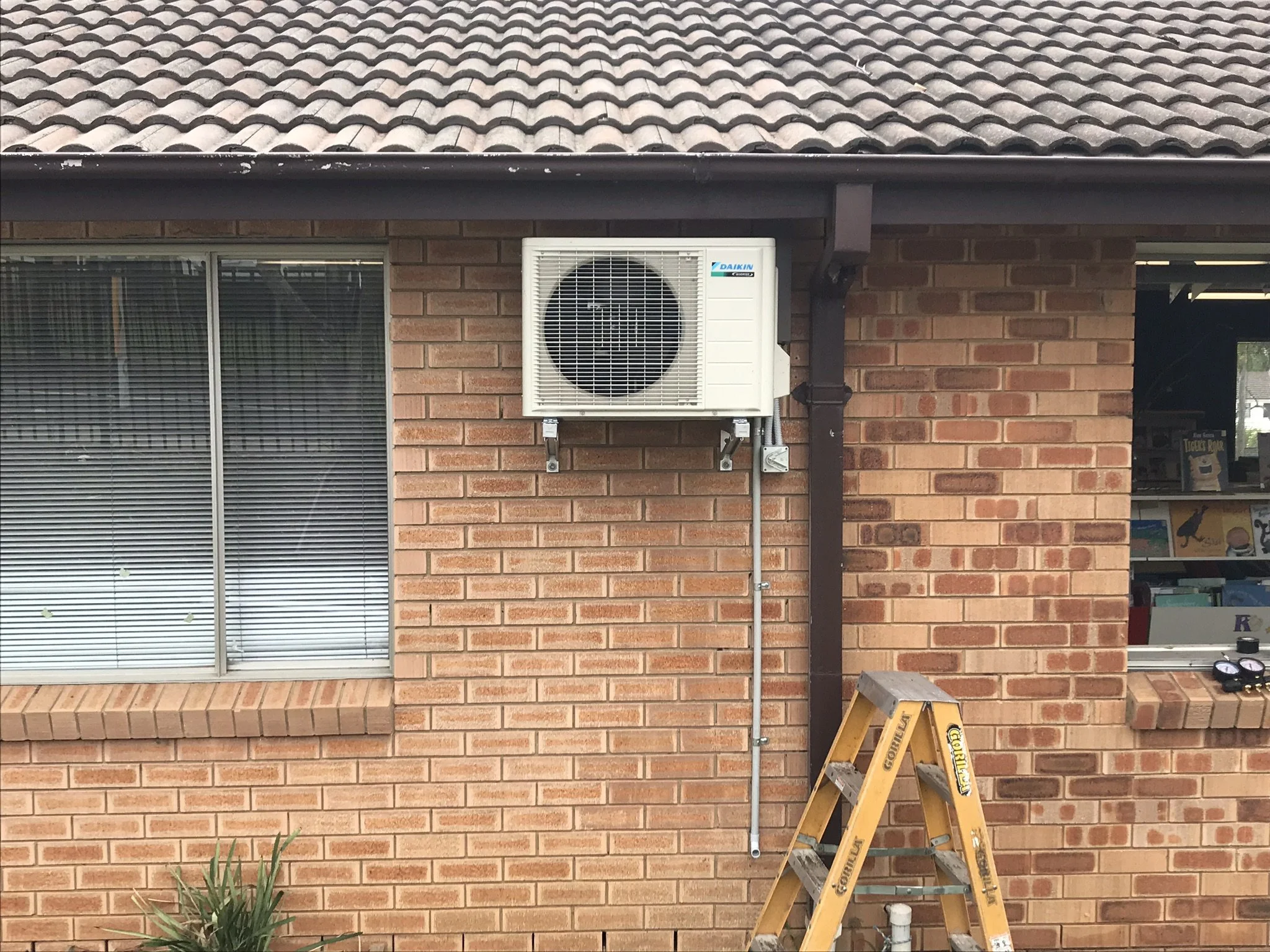 Split system outdoor unit on a brick wall, with a ladder below