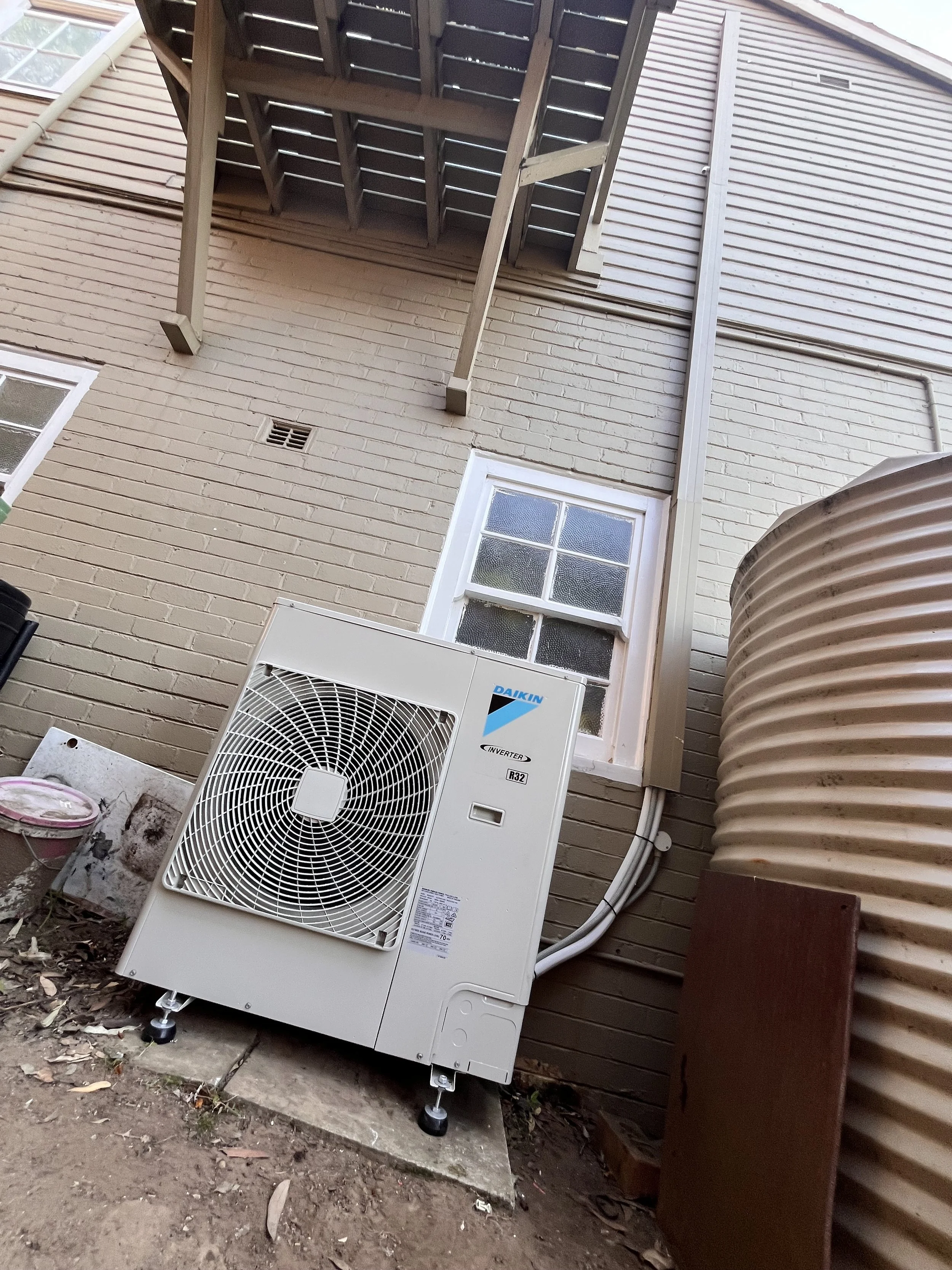 Daikin outdoor unit beside a weatherboard house and rainwater tank