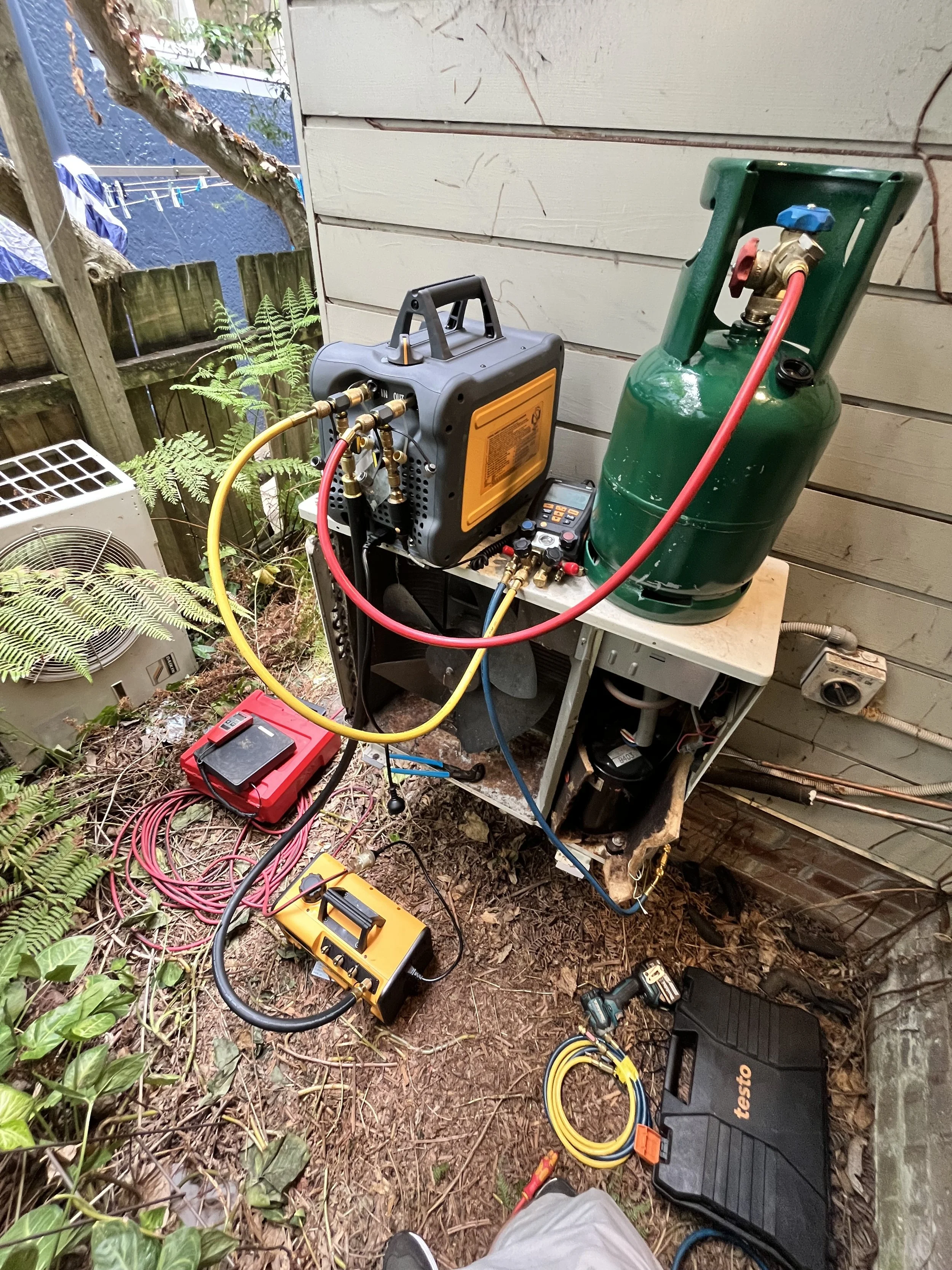 Refrigerant recovery machine and cylinder connected to an outdoor unit beside a house