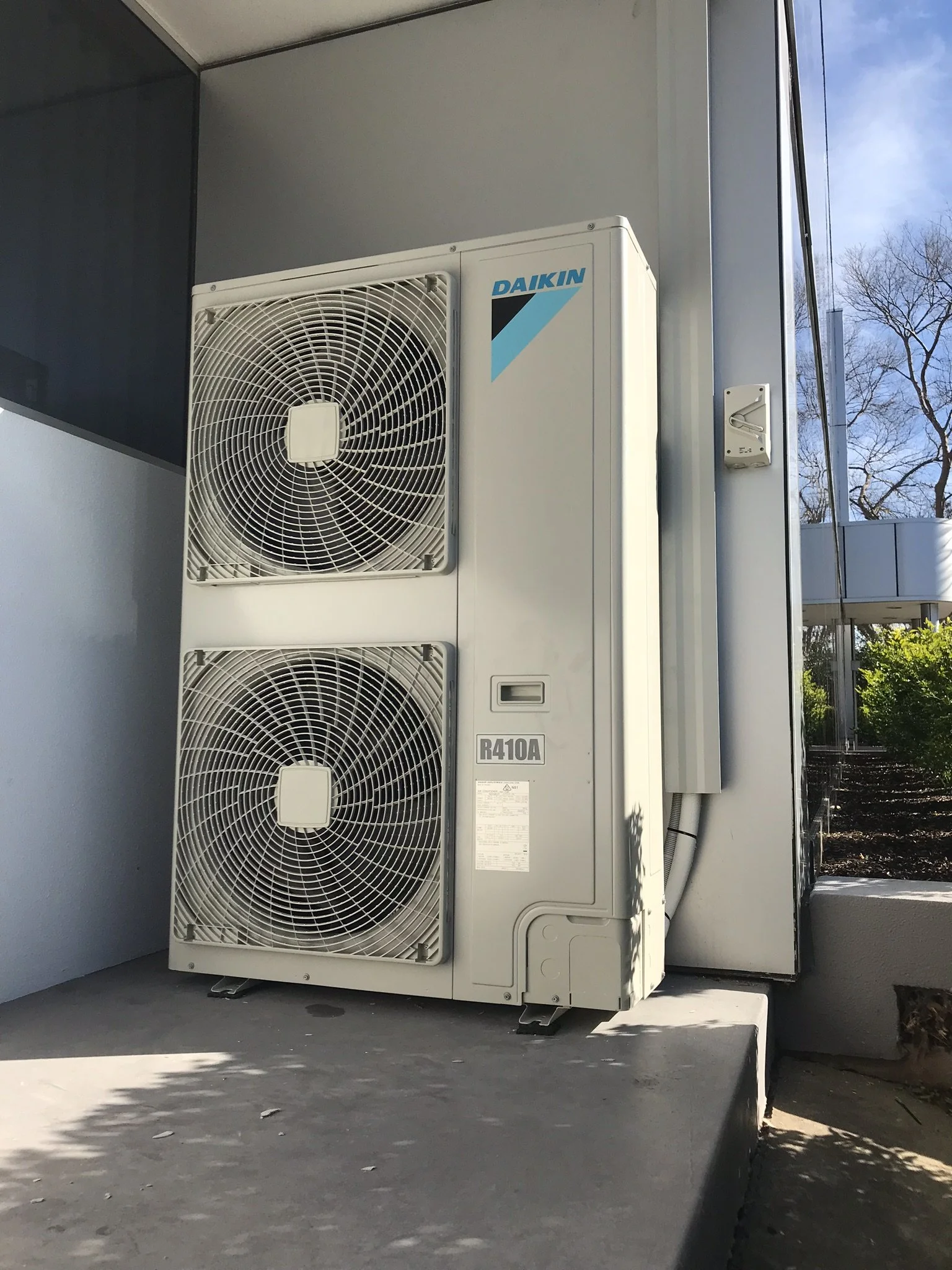 Daikin twin-fan outdoor unit on a concrete base beside a building