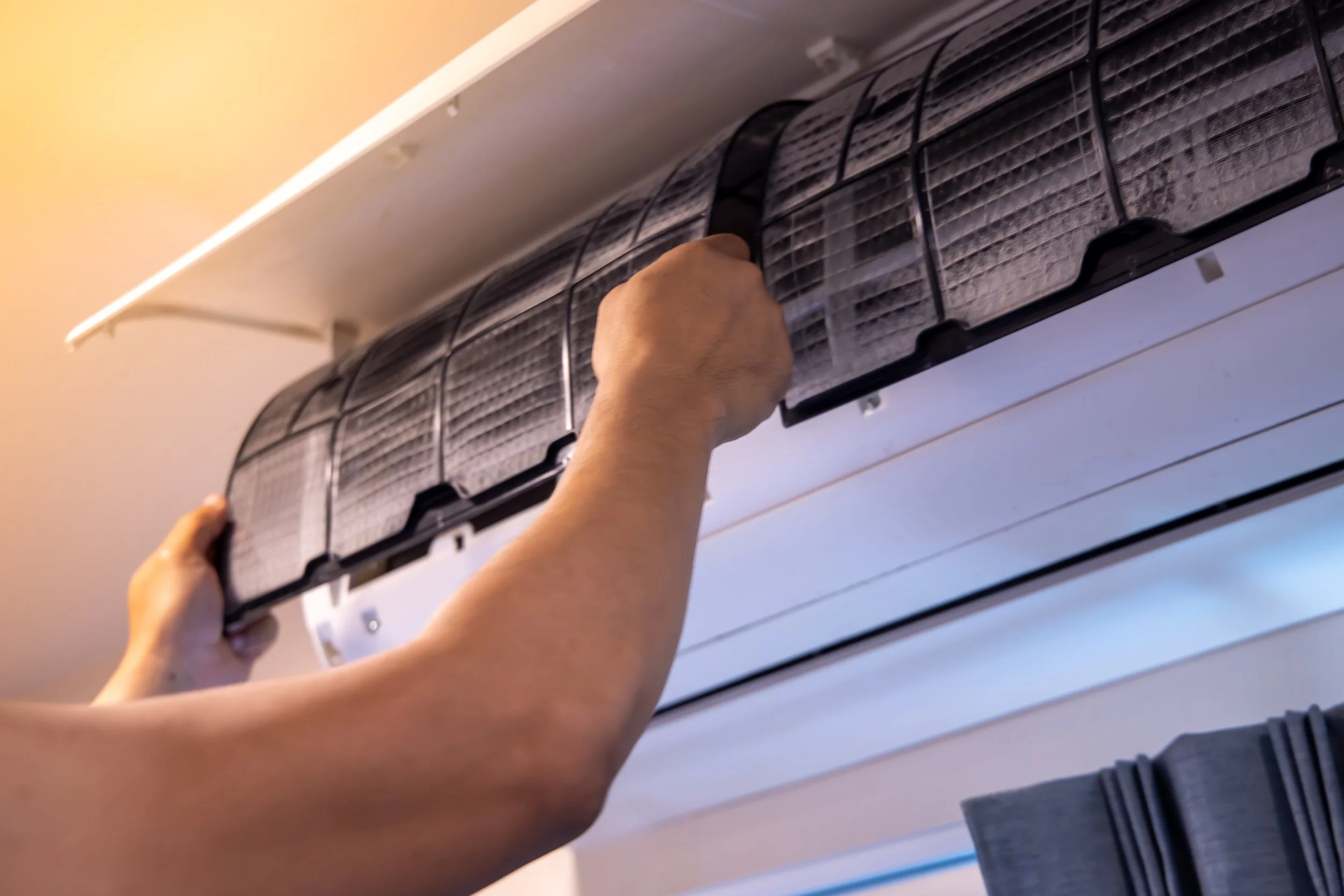 Person lifting an air filter to install it near an air conditioning unit.