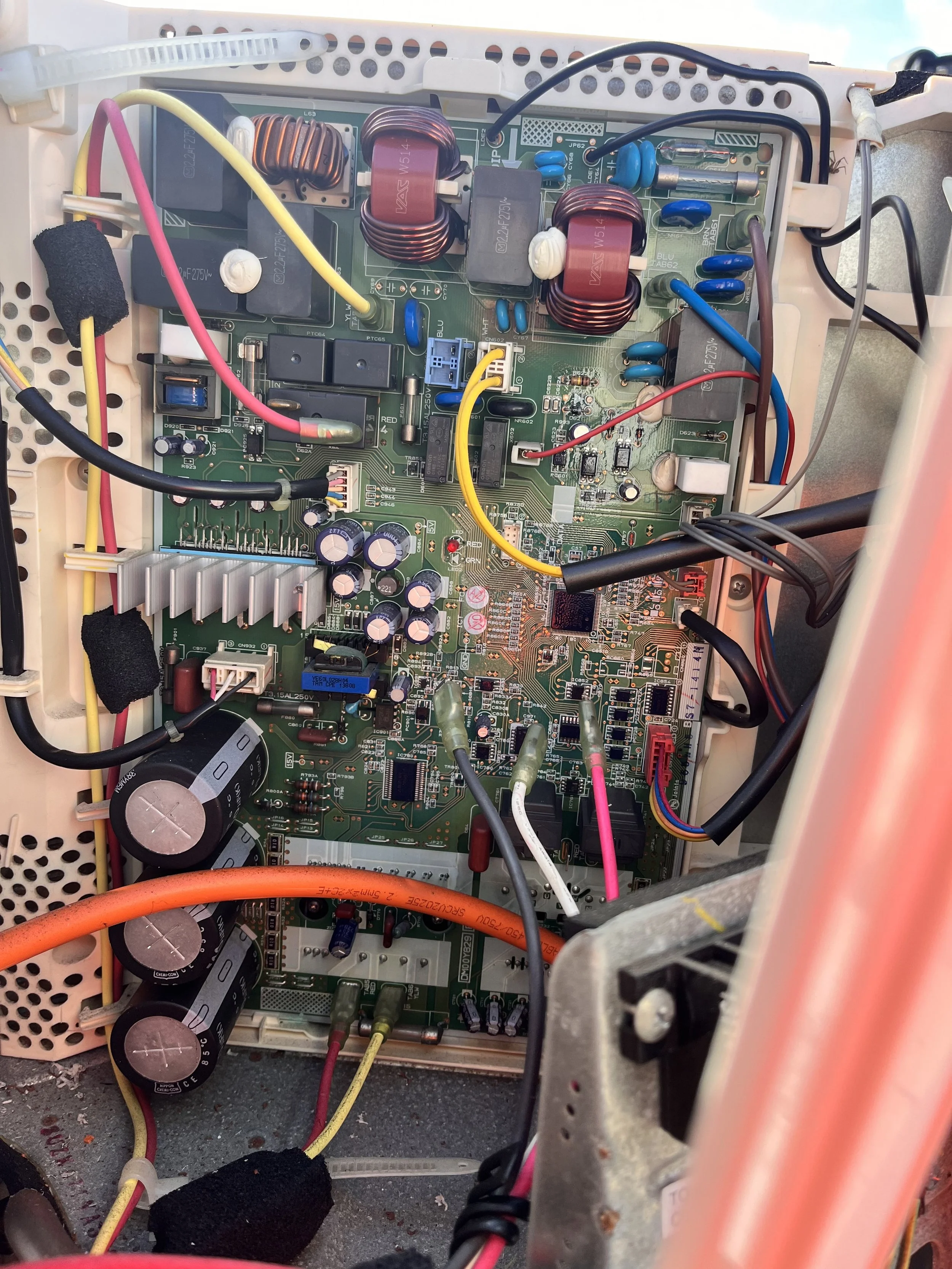Close-up of an electronic circuit board on a daikin air con with various capacitors, resistors, inductors, wires, and components inside a device or machine case.