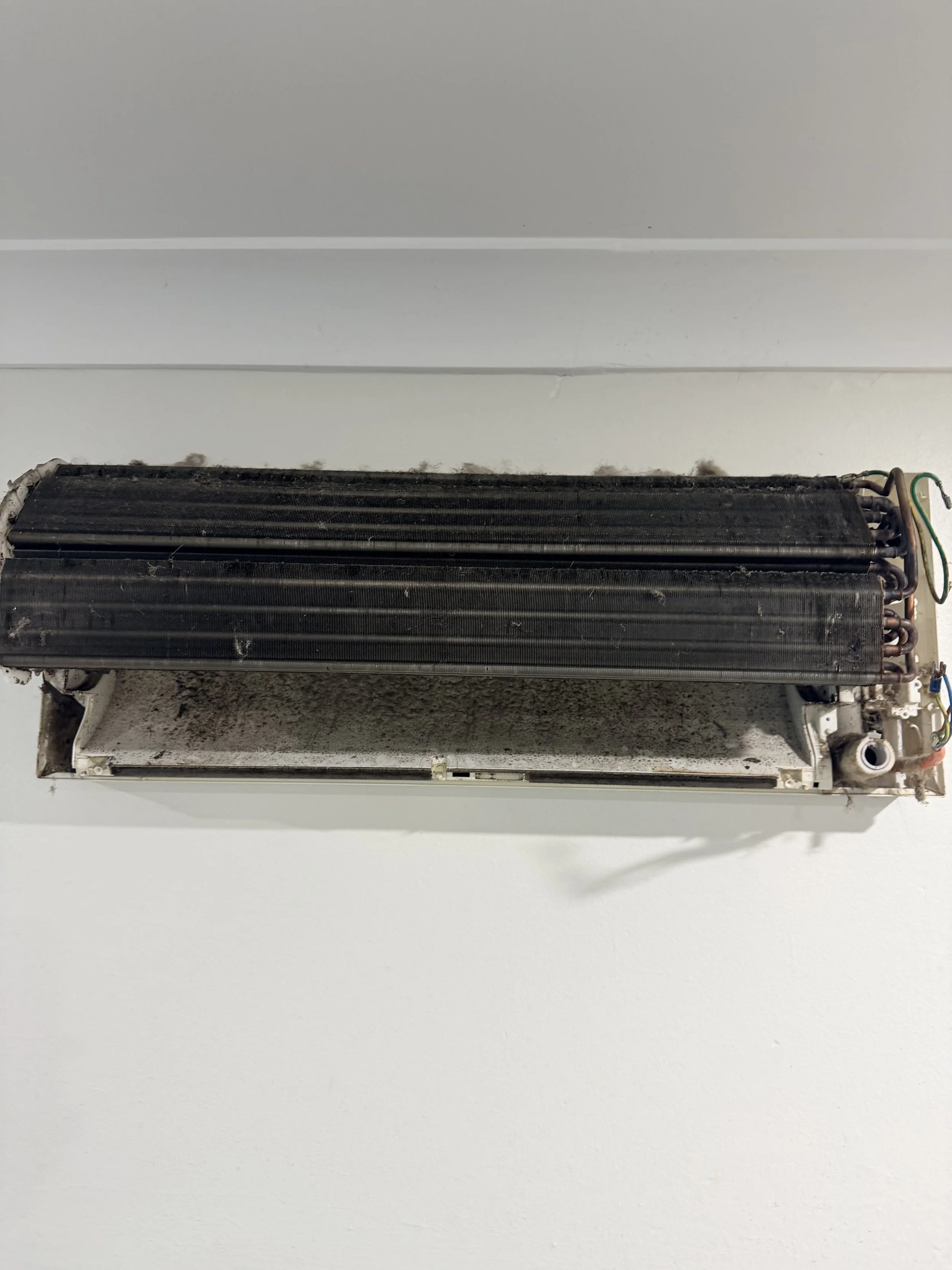Disassembled wall-mounted air conditioning unit with exposed internal components and wiring. Before Cleaning