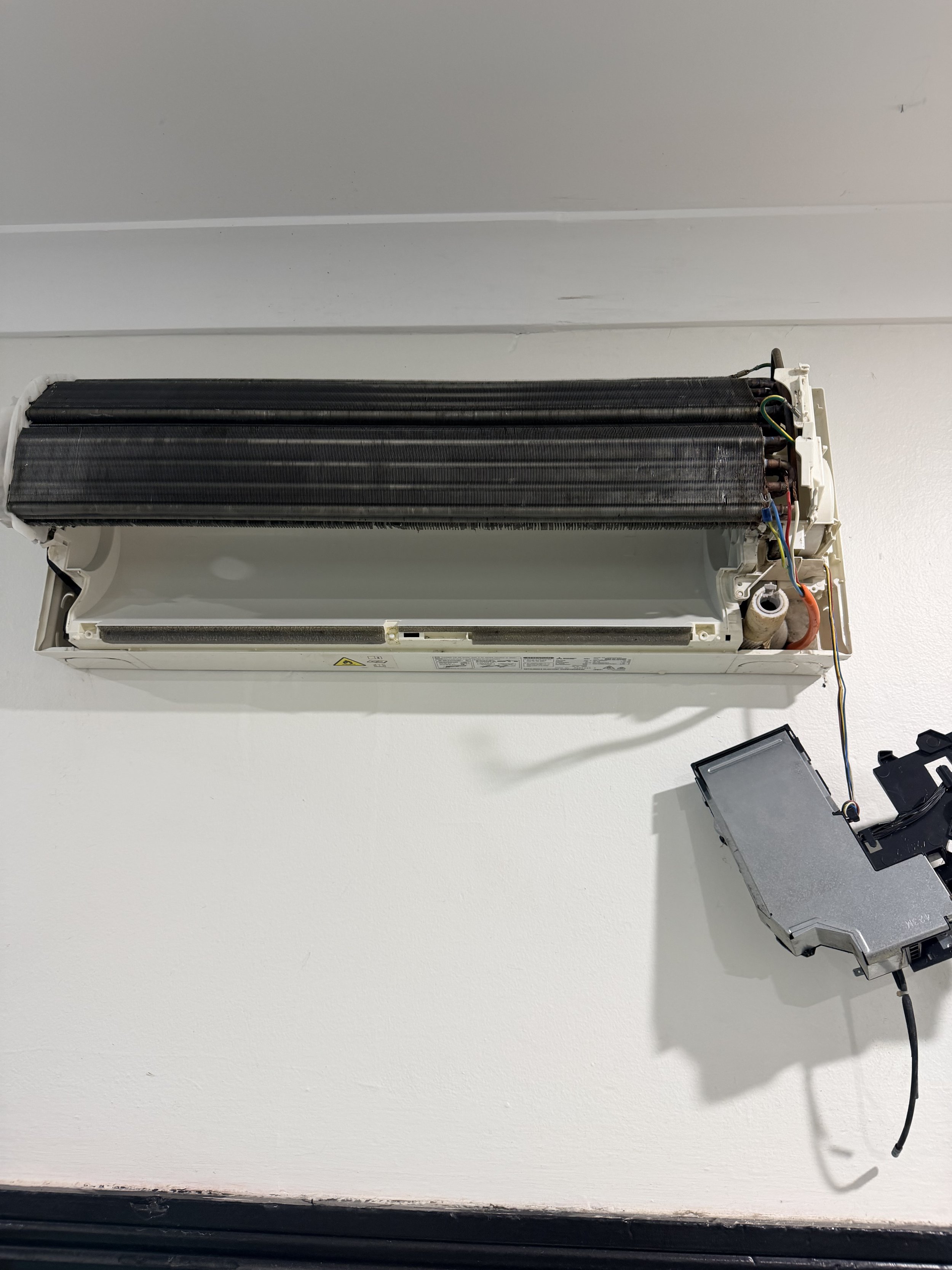 Disassembled wall-mounted air conditioning unit with exposed internal components and wiring. After Cleaning