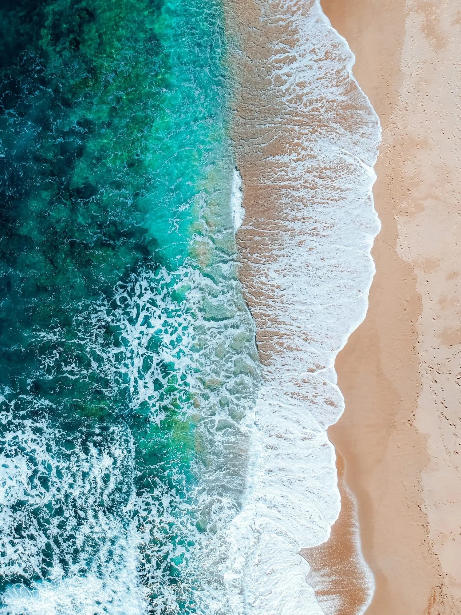 Aerial view of the ocean meeting a sandy beach, with waves crashing onto the shore.