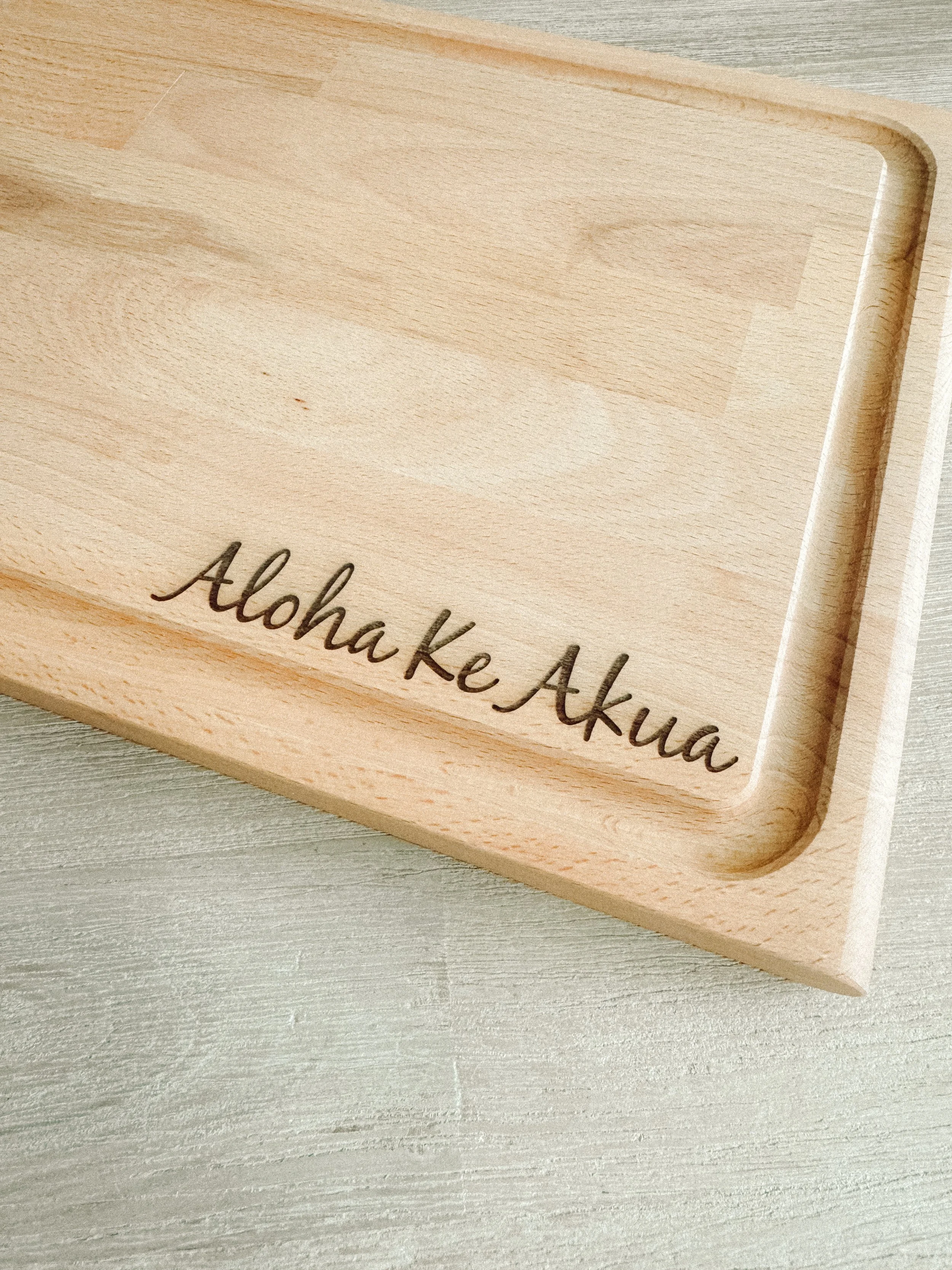 Close-up of a light-colored wooden cutting board with the words "Aloha Ke Akua" engraved on it made in Oahu Hawaii