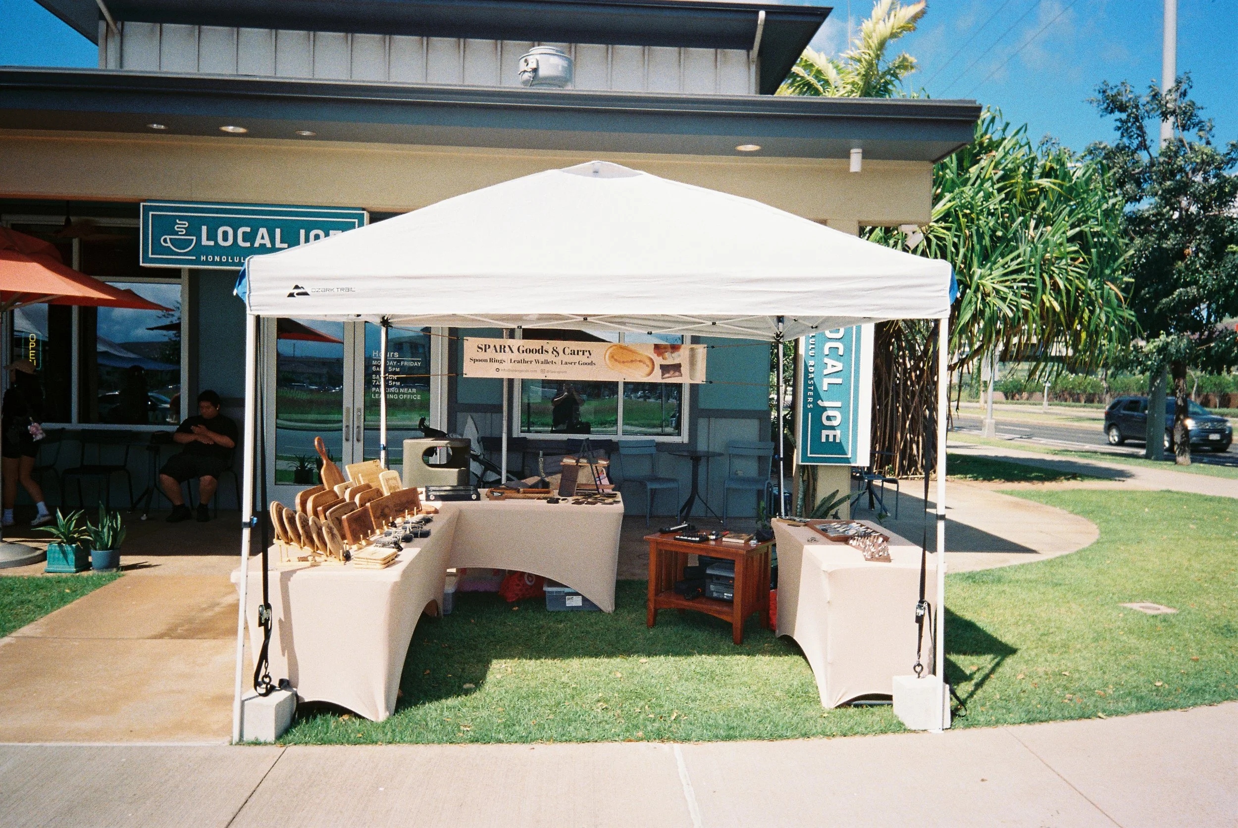 Outdoor market stall with jewelry and accessories displayed on tables under a white canopy in Oahu Hawaii
