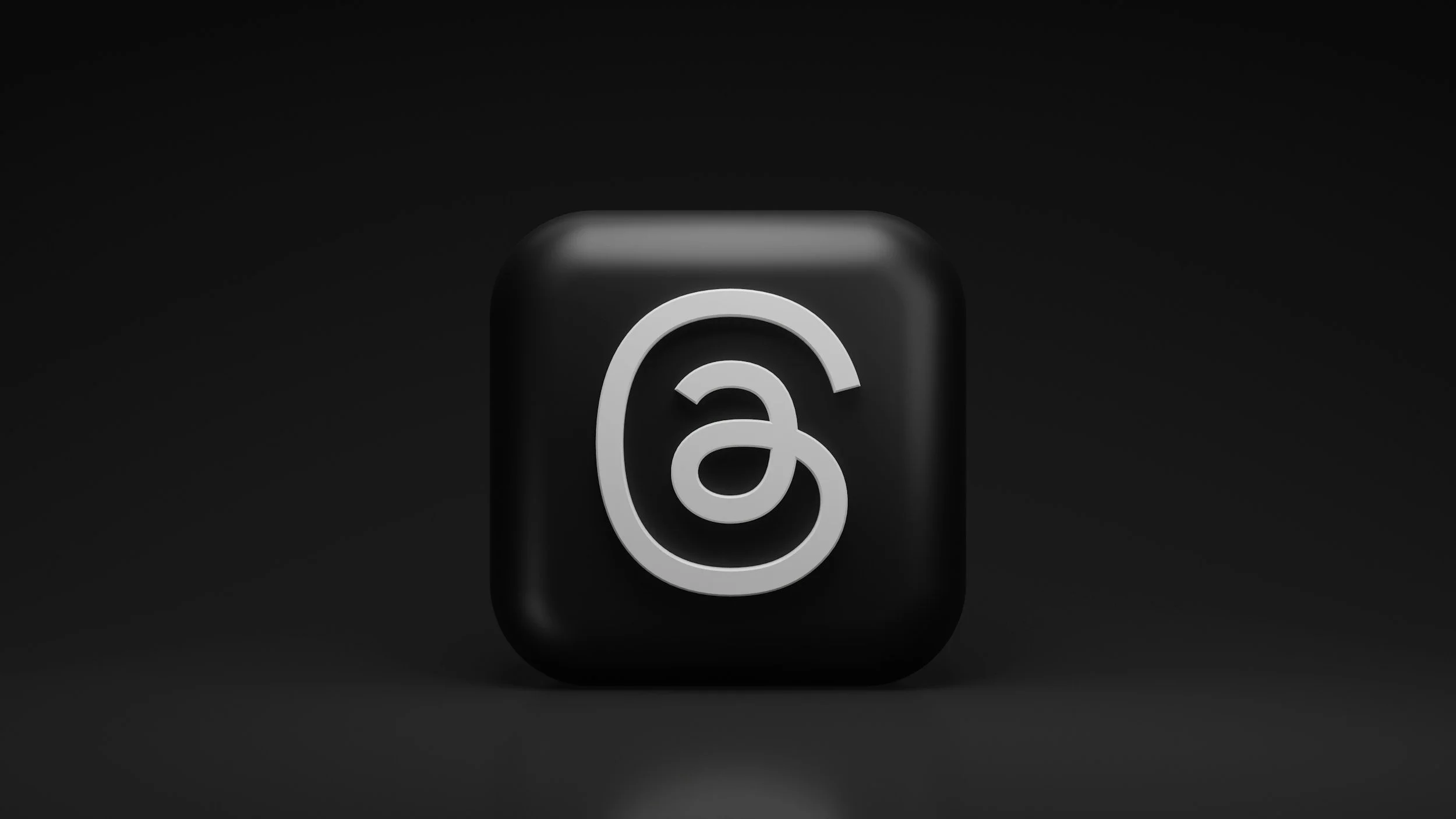 A black cube with a white social media logo on its front, set against a dark background.