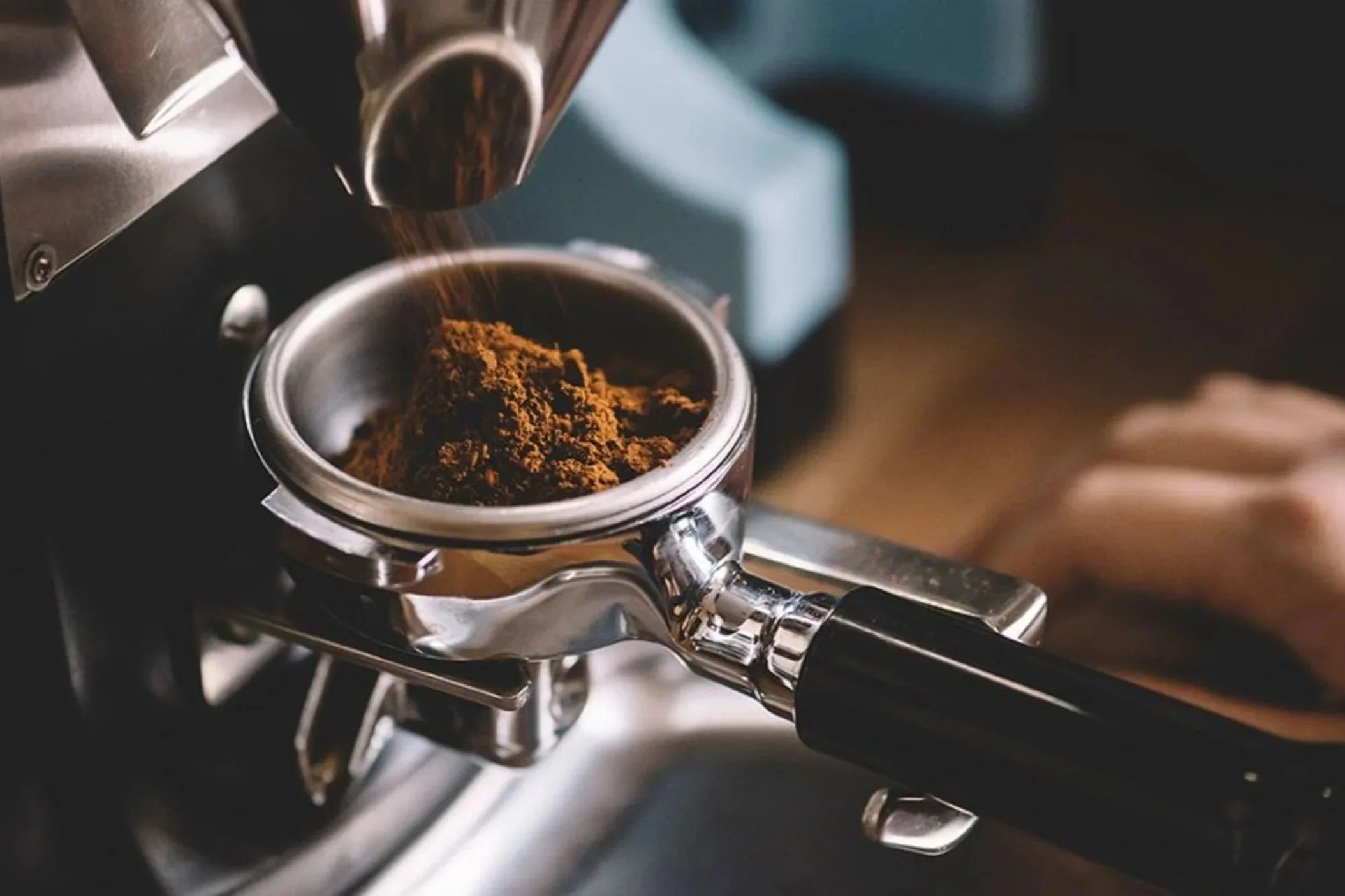 Close-up of an espresso machine pouring espresso into a metal cup, with a splash of coffee grounds on top.