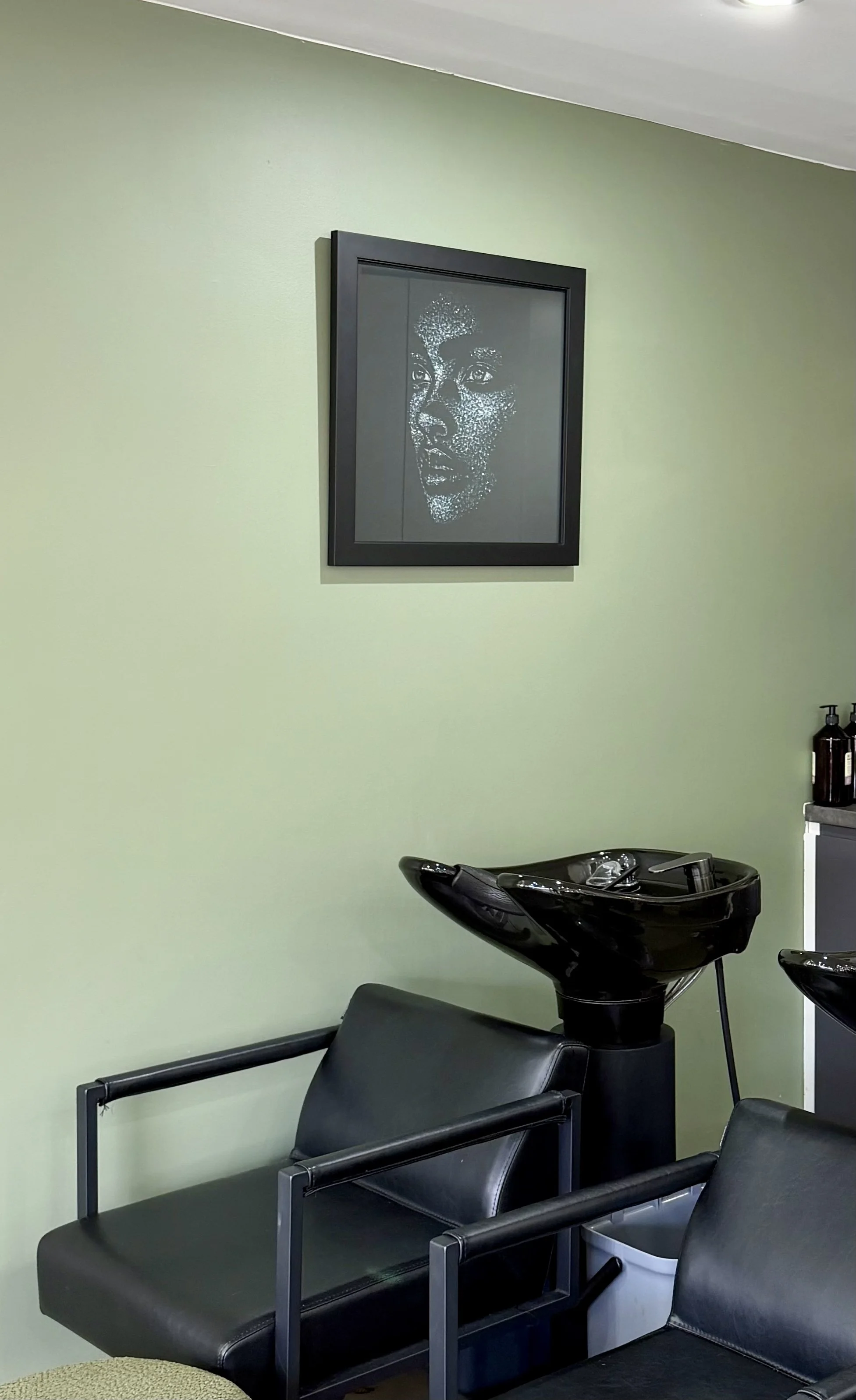 Backwash basin area at Janos Kiss Hair in Cremorne, with black reclining wash chairs, a sage green wall and framed artwork