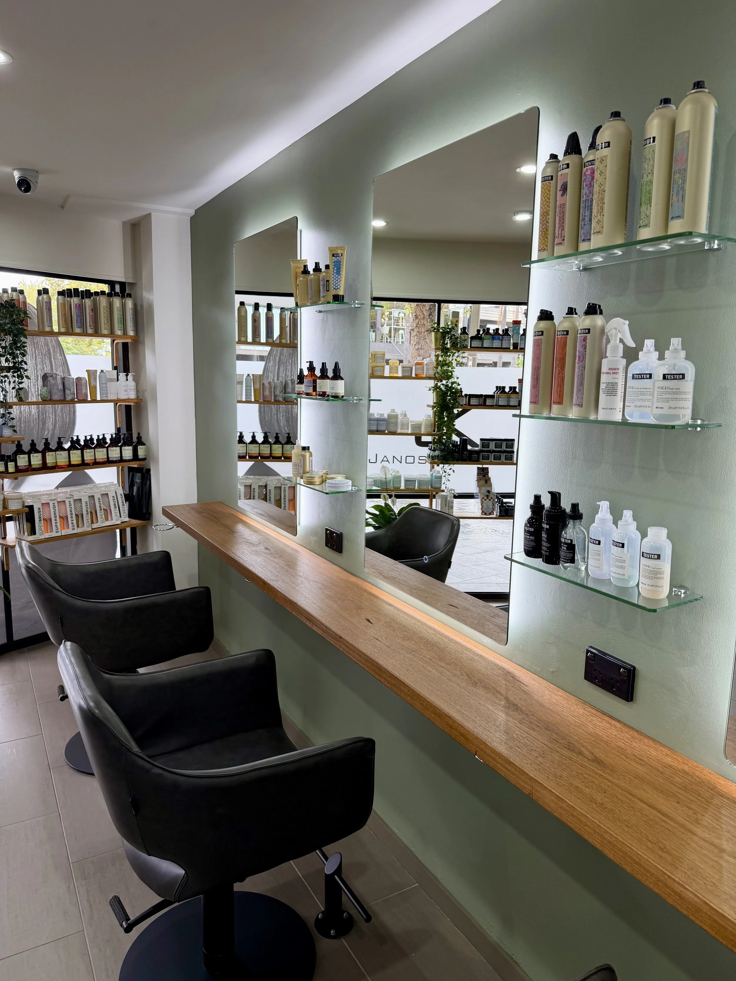 Styling stations at Janos Kiss Hair in Cremorne, with backlit mirrors, a timber bench and shelves of Davines hair care products