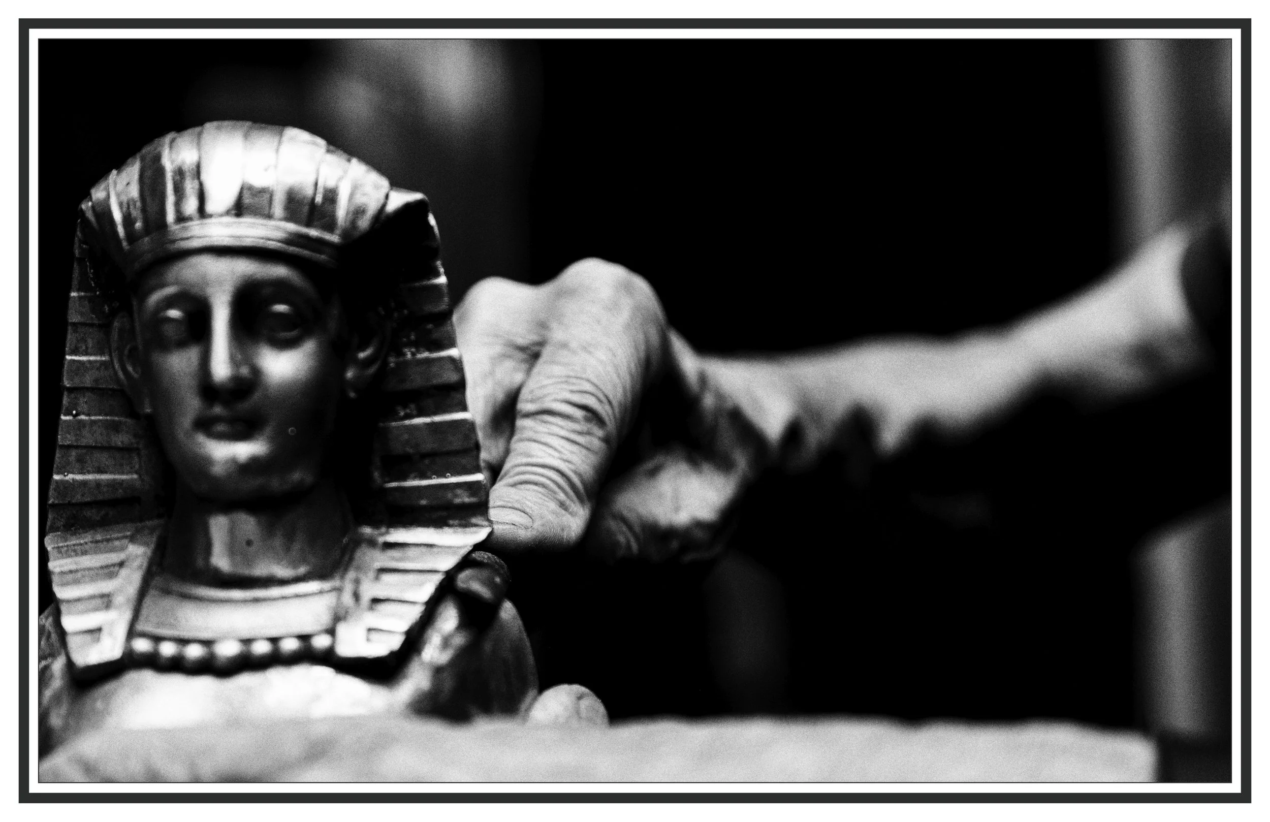 Close-up of a person's hand carving a small sculpture of a face with a chisel. The sculpture features detailed facial features and a head covering, with the face looking straight ahead.