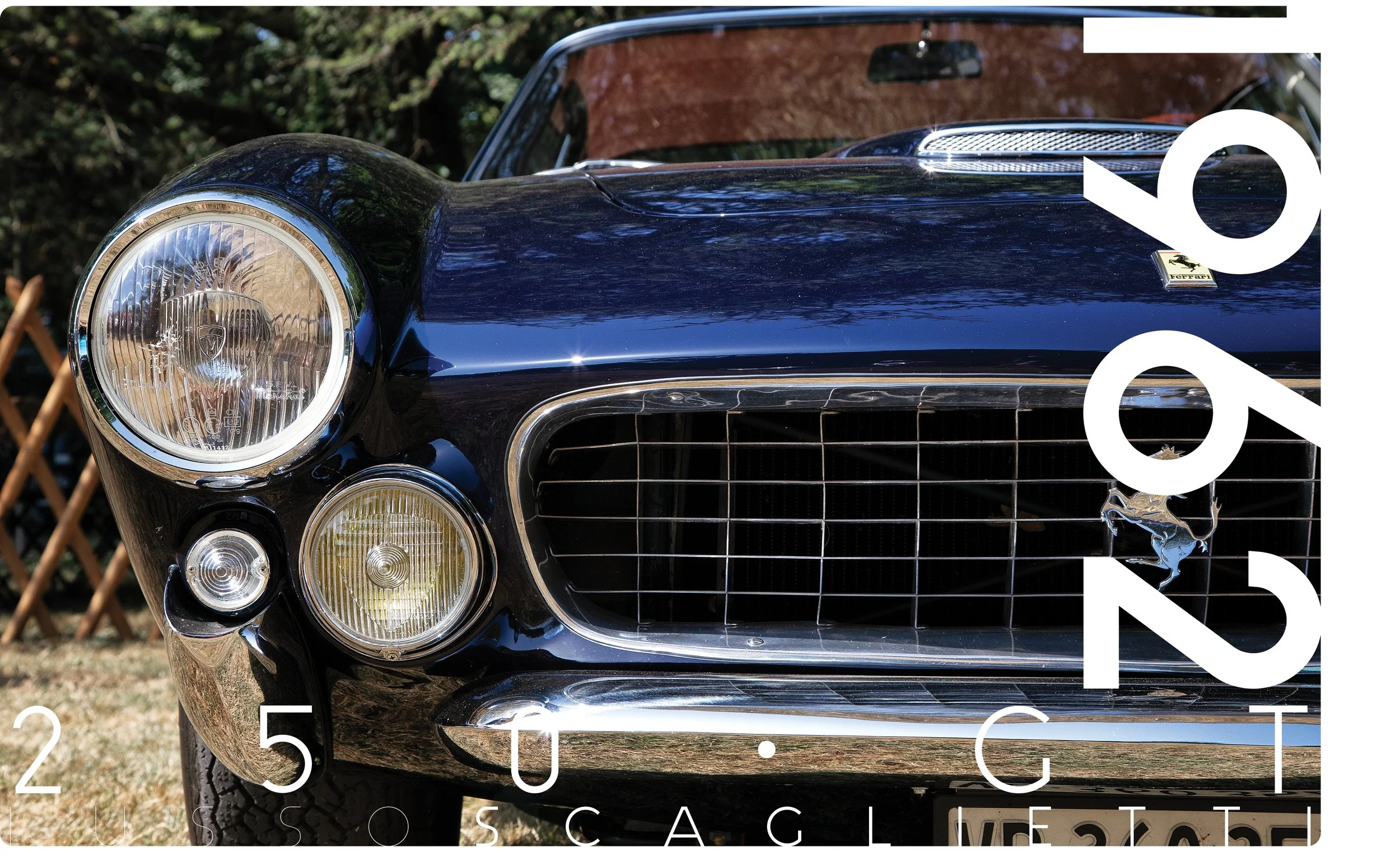Close-up of a vintage black Ferrari car's front, showcasing a large round headlight, a smaller light below, the Ferrari emblem, and a chrome grille, with a background of trees and a wooden fence.
