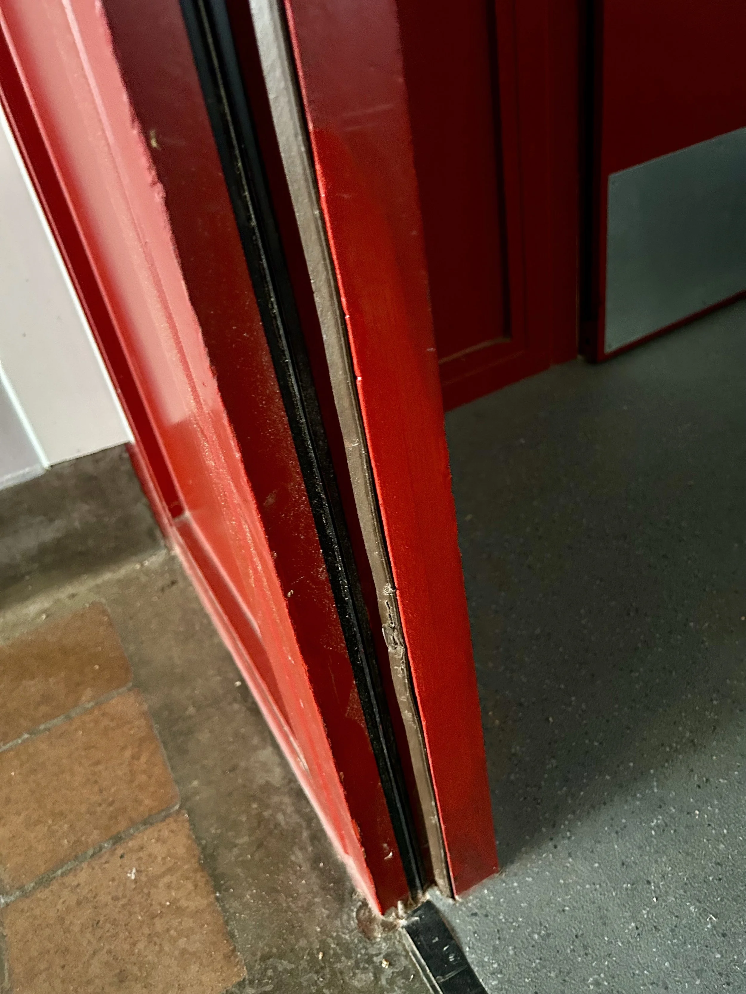 Close-up of a damaged red metal door frame and threshold.
