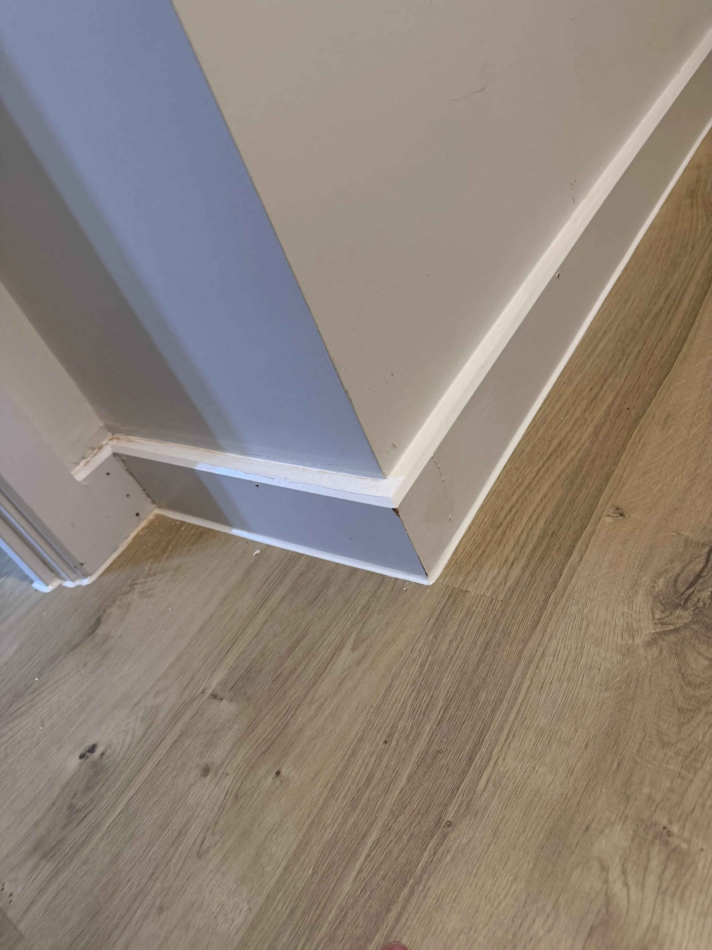 Close-up of a white-painted window frame and blue-gray wall above a light wood floor.