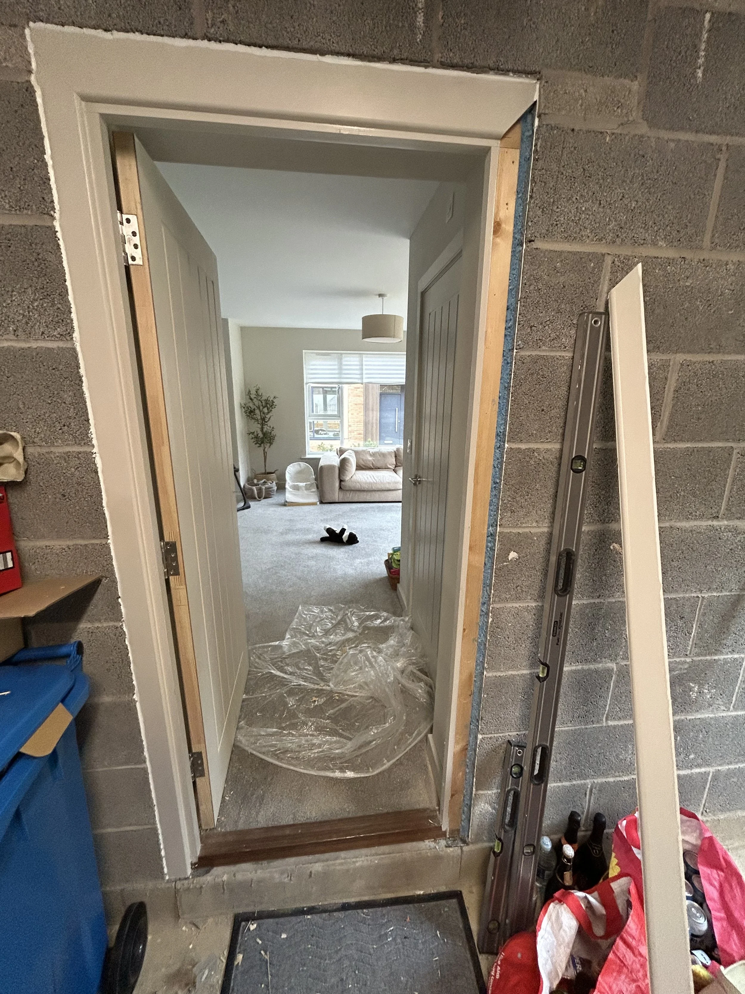 Partially finished doorway in a cinder block wall, opening into a carpeted living room with a sofa and window.
