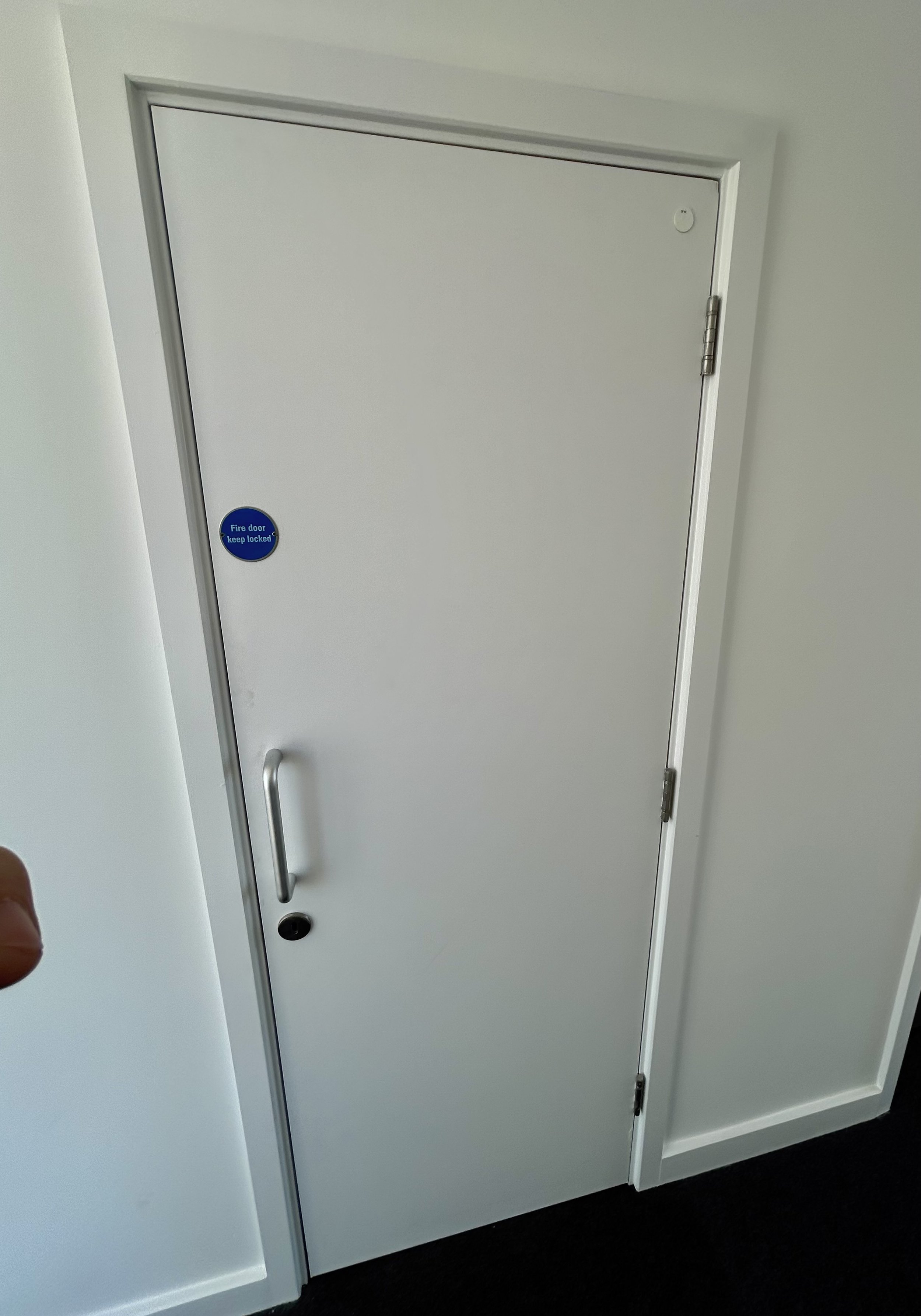 Closed white fire door with a blue “Fire door keep locked” sign, handle, and hinges.
