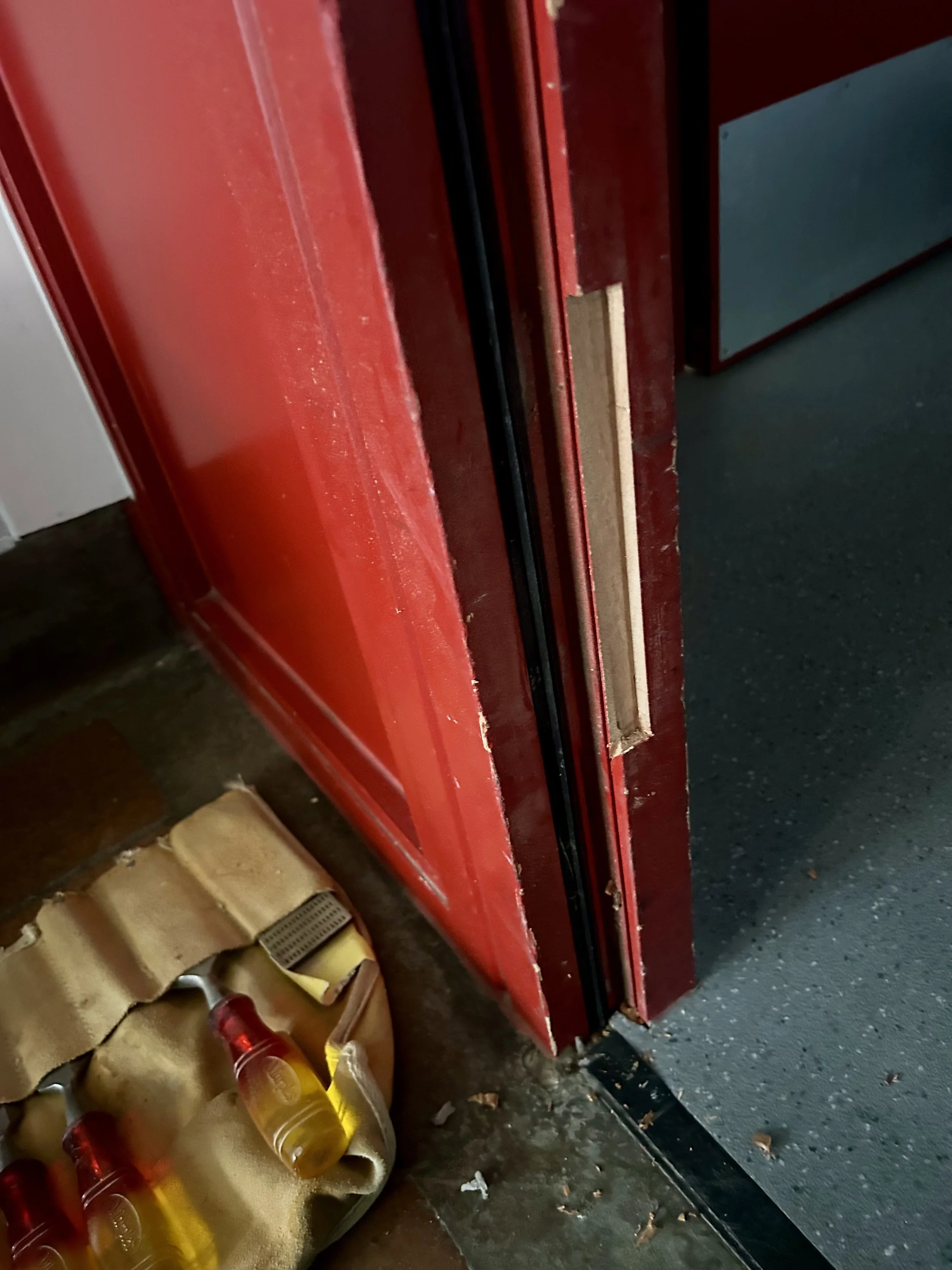 Close-up of a damaged red door or vehicle panel beside a cardboard box and plastic bottles.