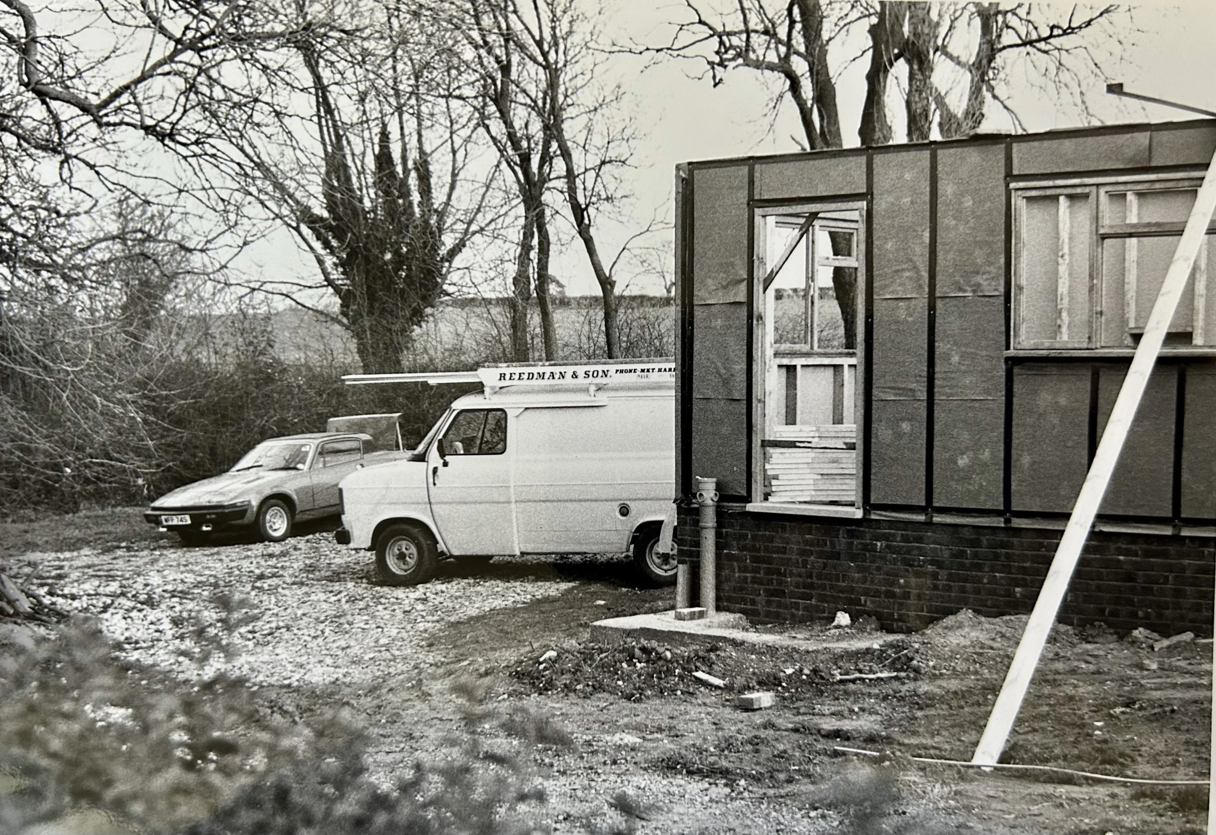 Black-and-white photo of a Redman & Son van parked beside a partially renovated house in a wooded yard.