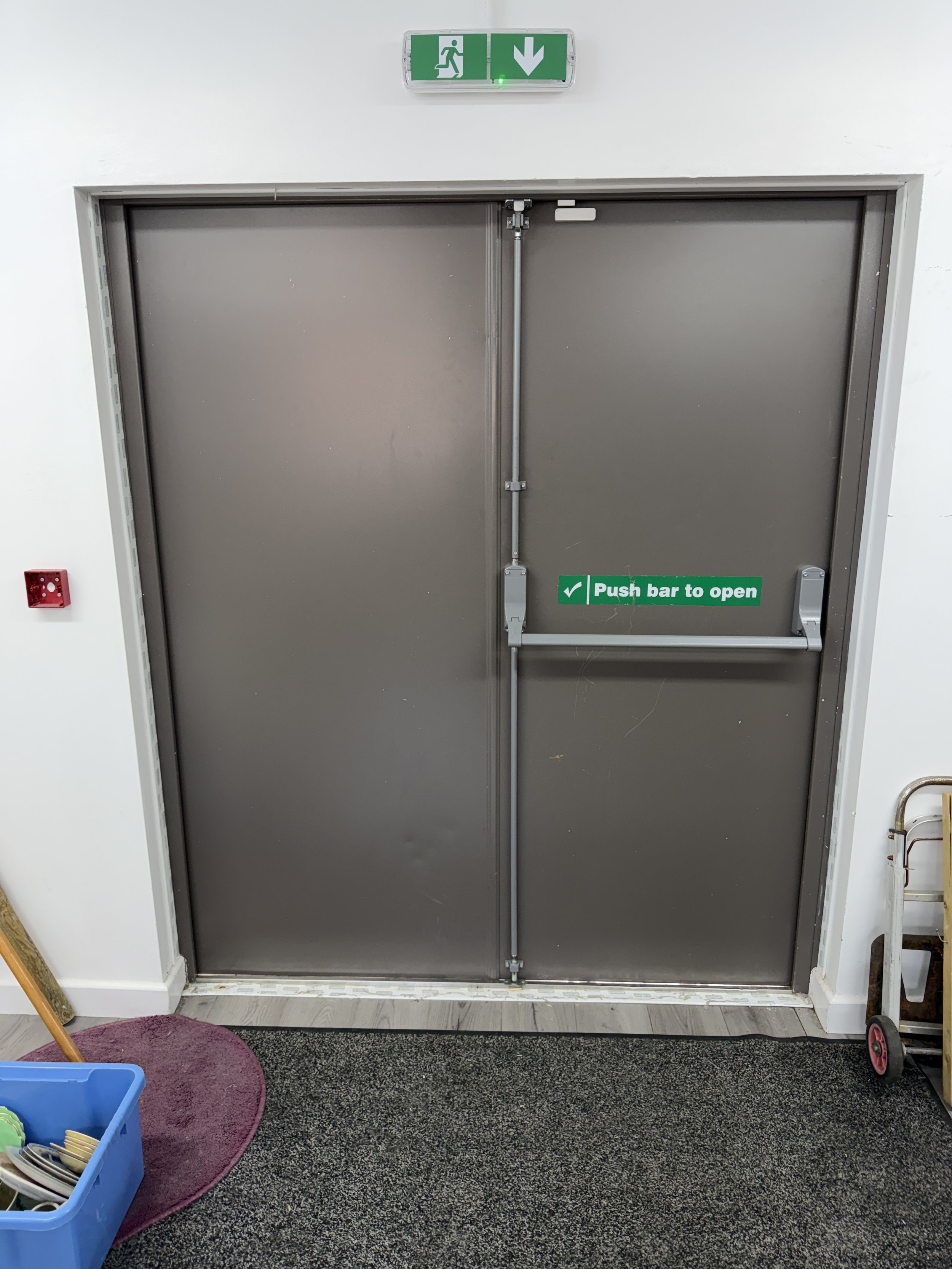 Gray emergency exit double doors with push bars and illuminated green exit sign