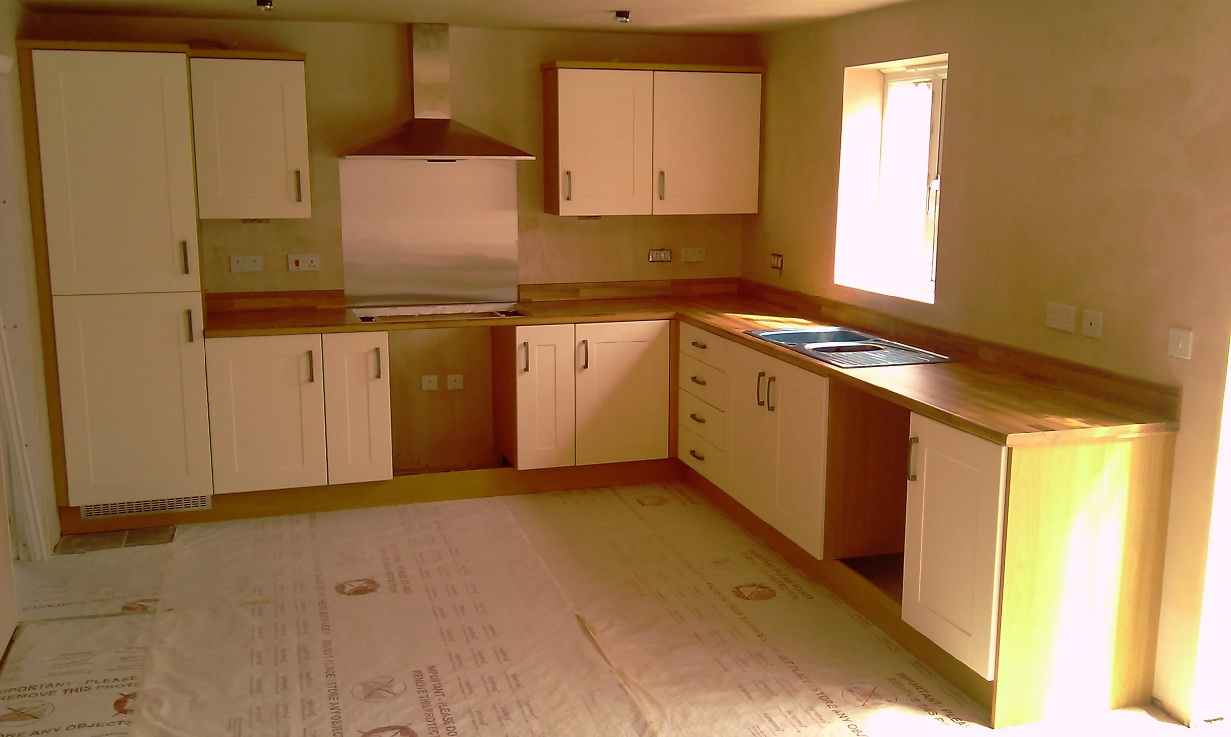 Newly renovated kitchen with white cabinets, wood countertops, range hood, and stainless-steel sink.