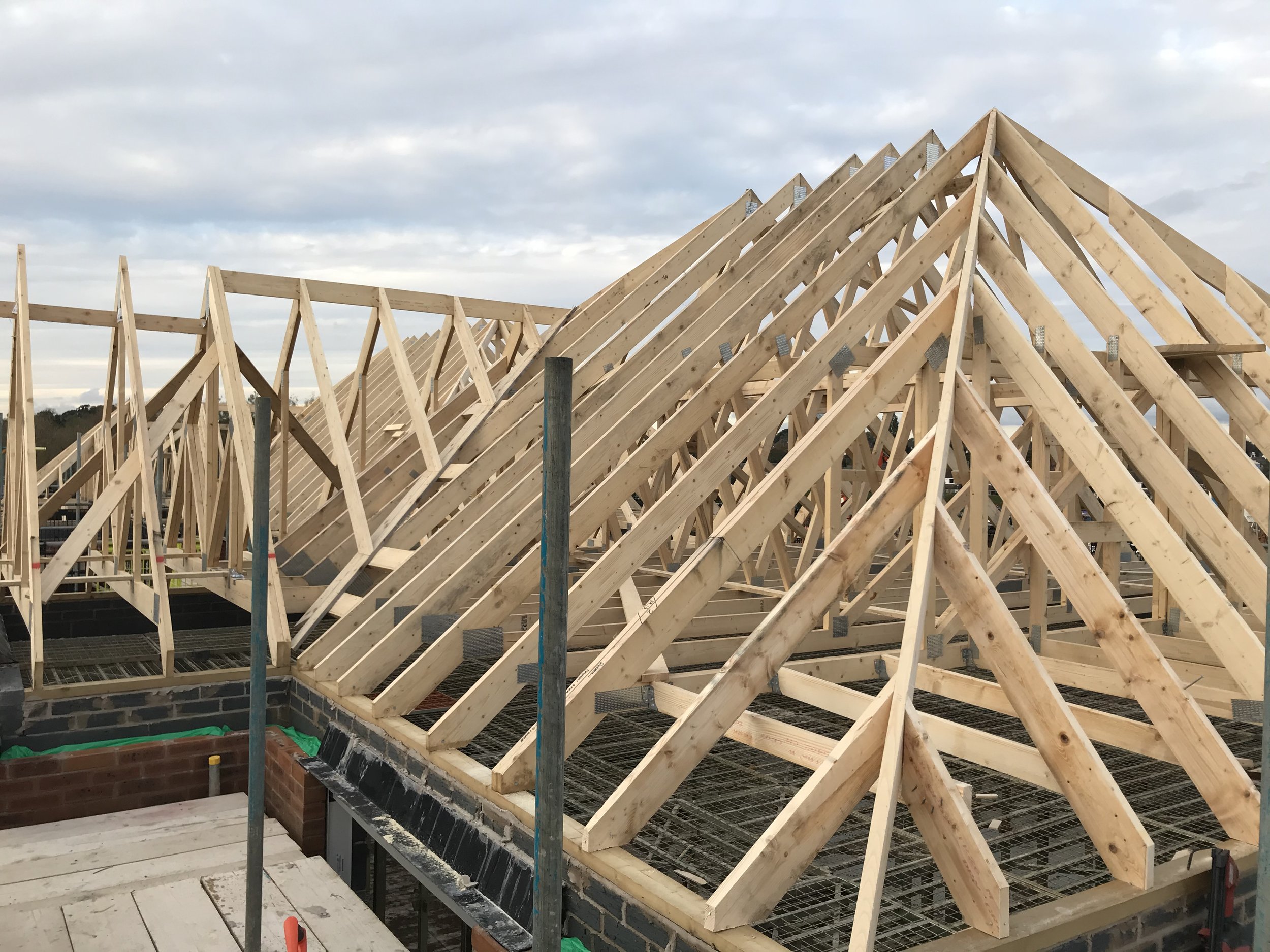Wooden roof trusses under construction on a brick house with scaffolding.