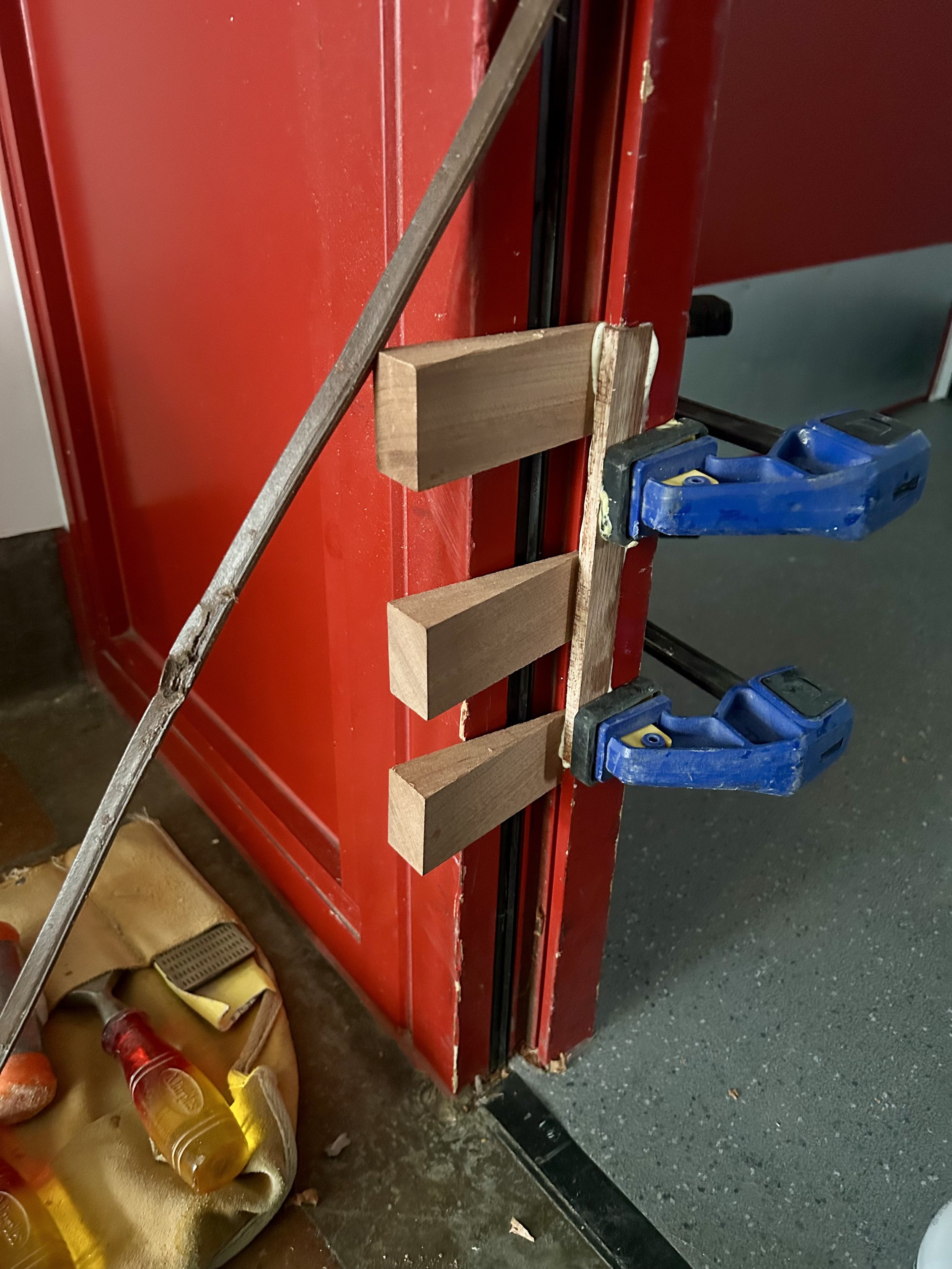 Close-up of a red metal door with wooden braces and blue clamps in a workshop