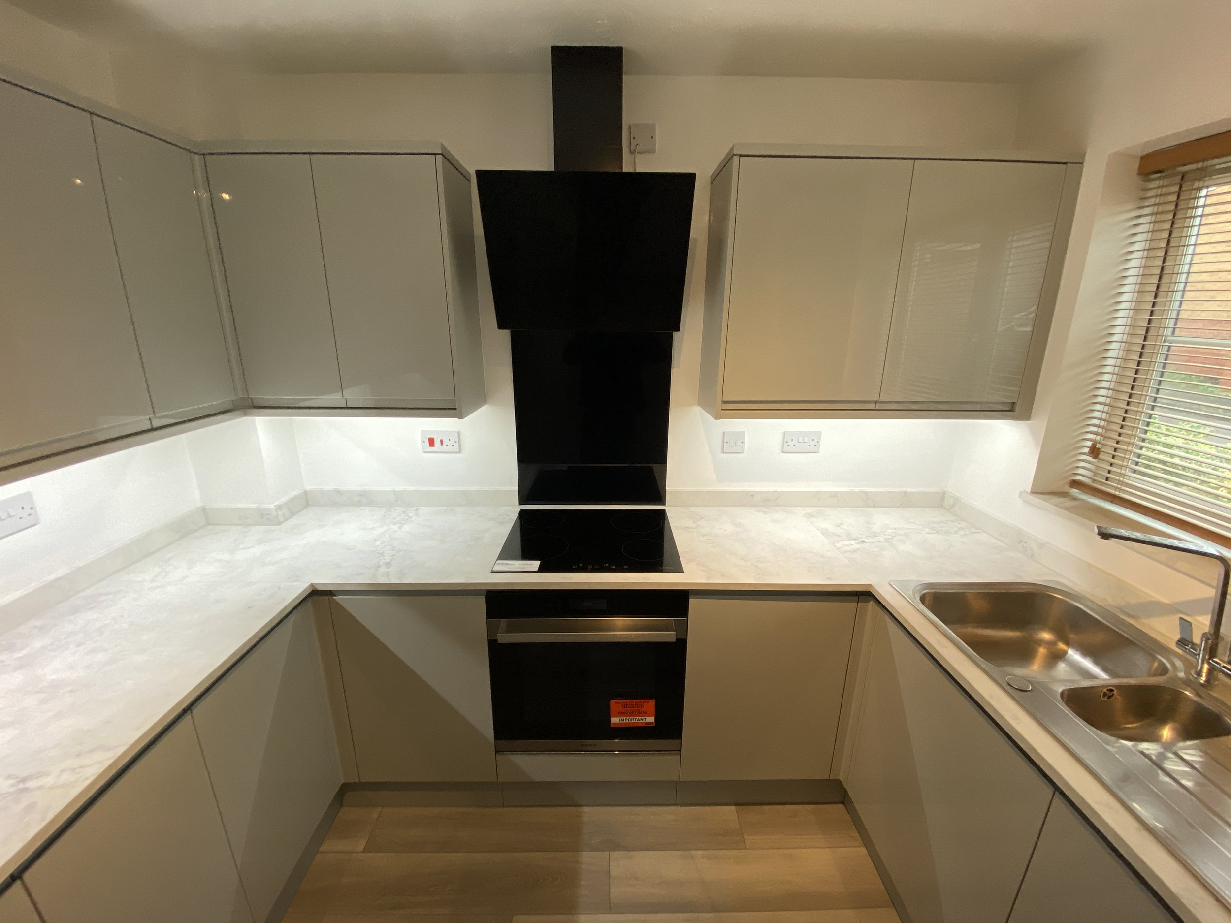 Modern U-shaped kitchen with white cabinets, marble-look countertops, black induction cooktop, built-in oven, range hood, and double stainless-steel sink.