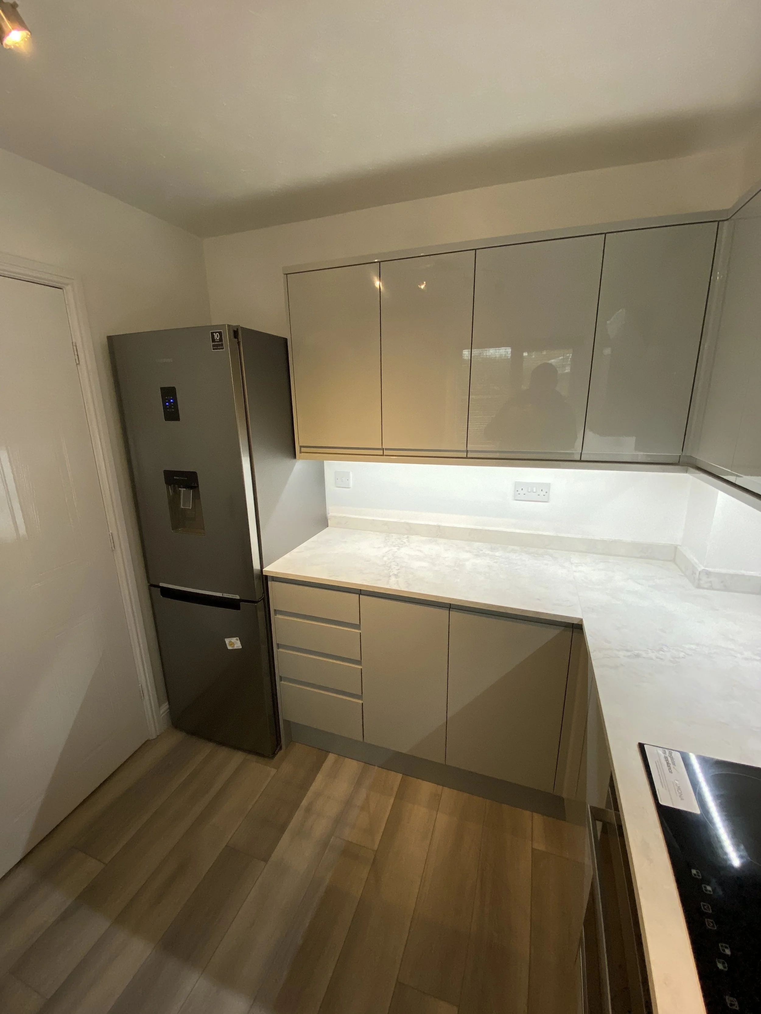 Modern kitchen with gray refrigerator, glossy cabinets, white marble countertops, and wood flooring