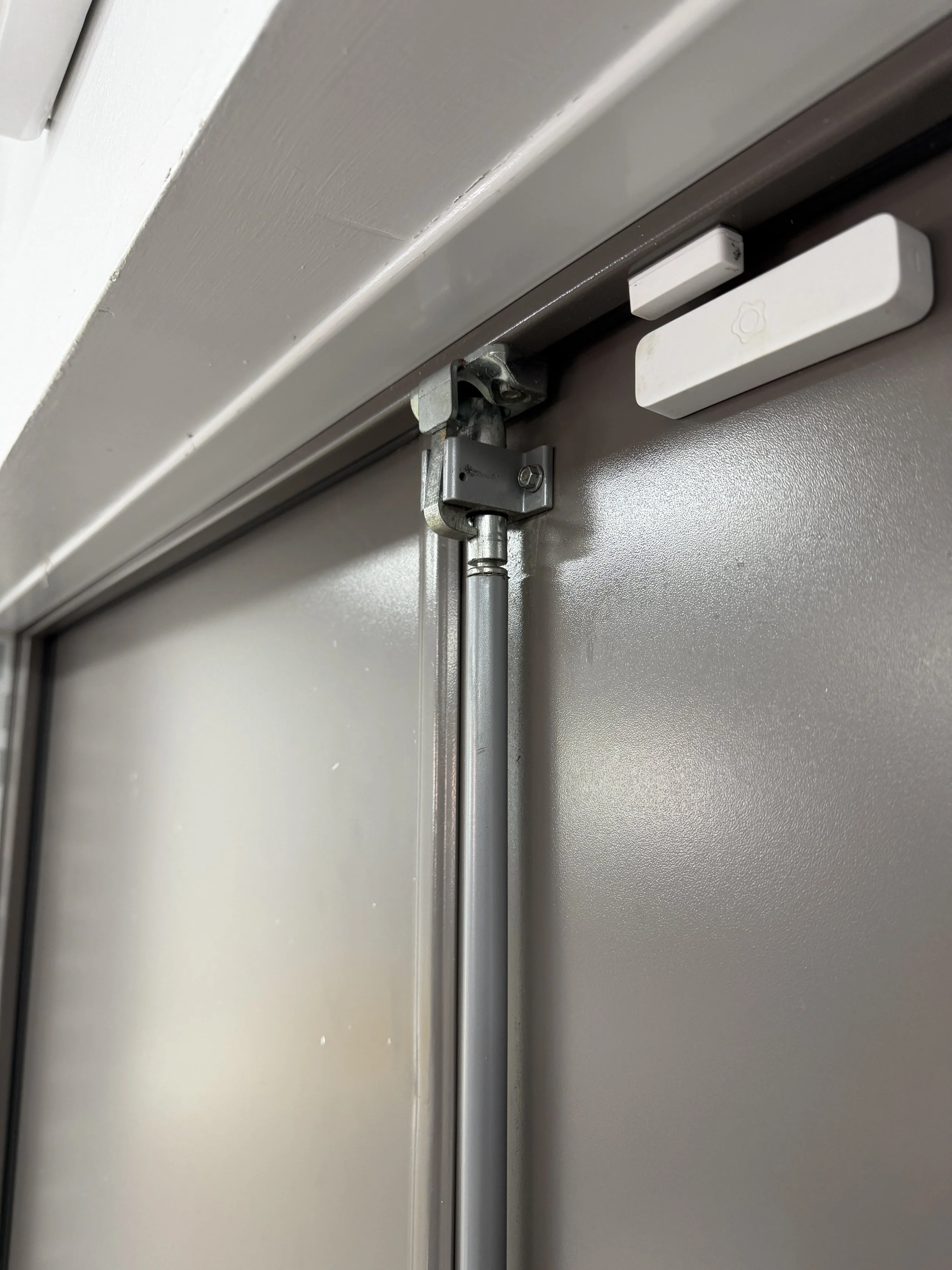 Close-up of a commercial door’s overhead closer, hinge, and white door hardware
