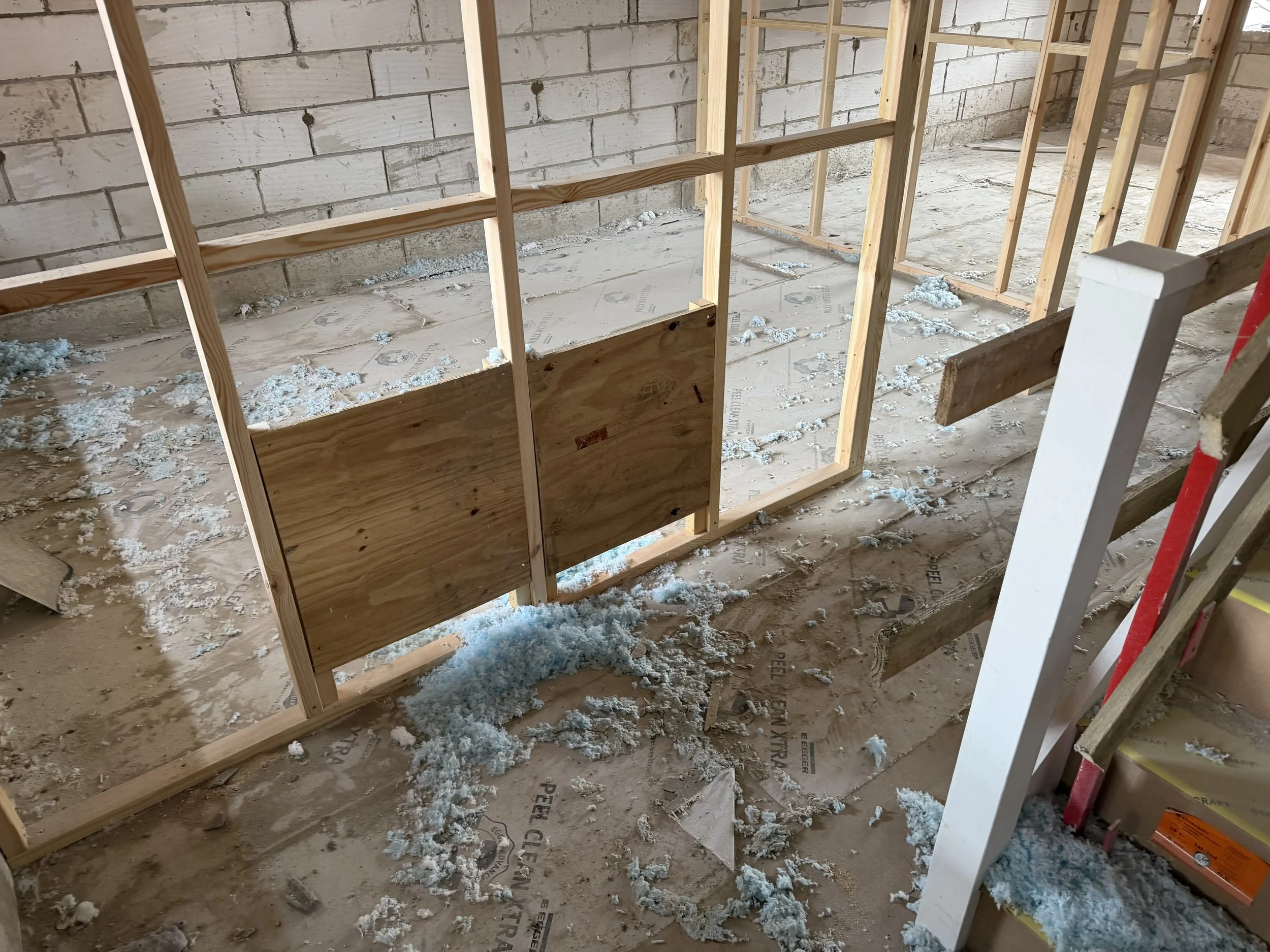Unfinished basement with exposed wood framing, concrete block walls, floor insulation, and scattered fiberglass insulation.