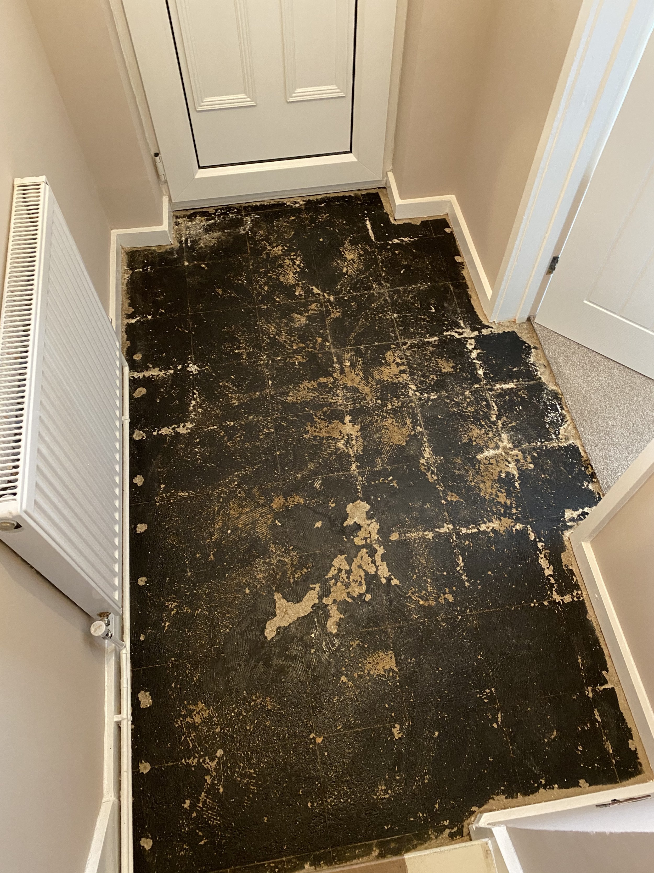 Worn black hallway floor with peeling adhesive residue, white doors, baseboards, and a radiator.